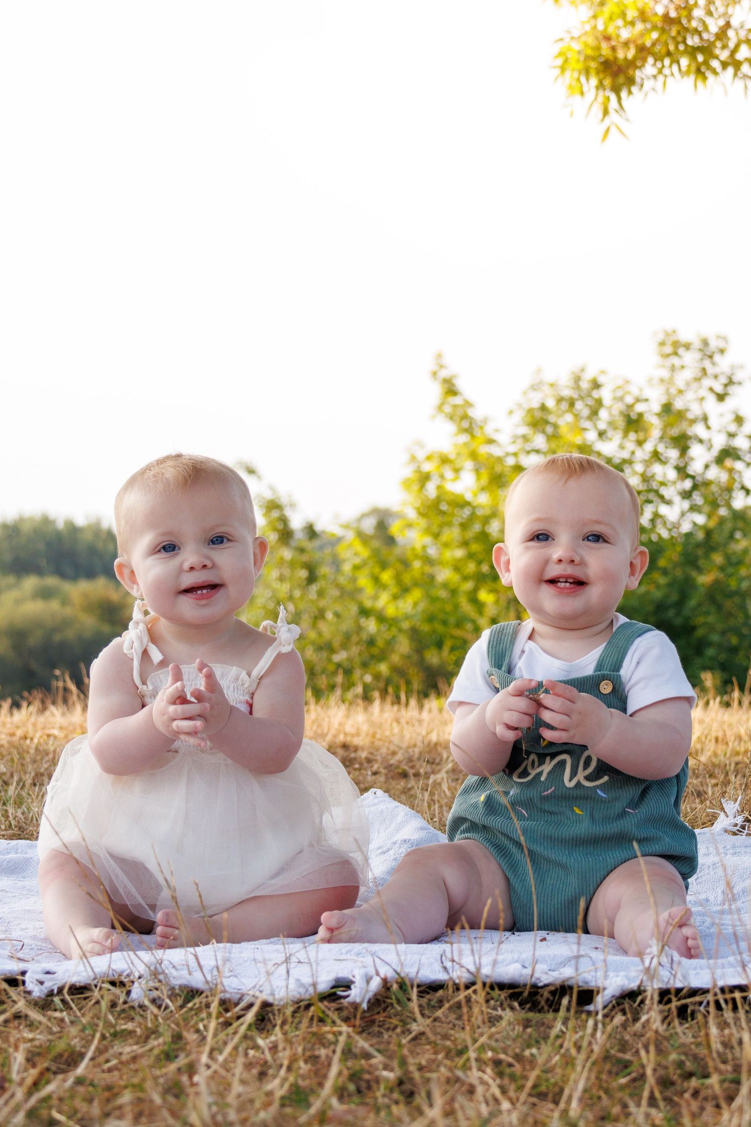 A series of outdoor baby portraits on a white blanket in a grassy field at golden hour.