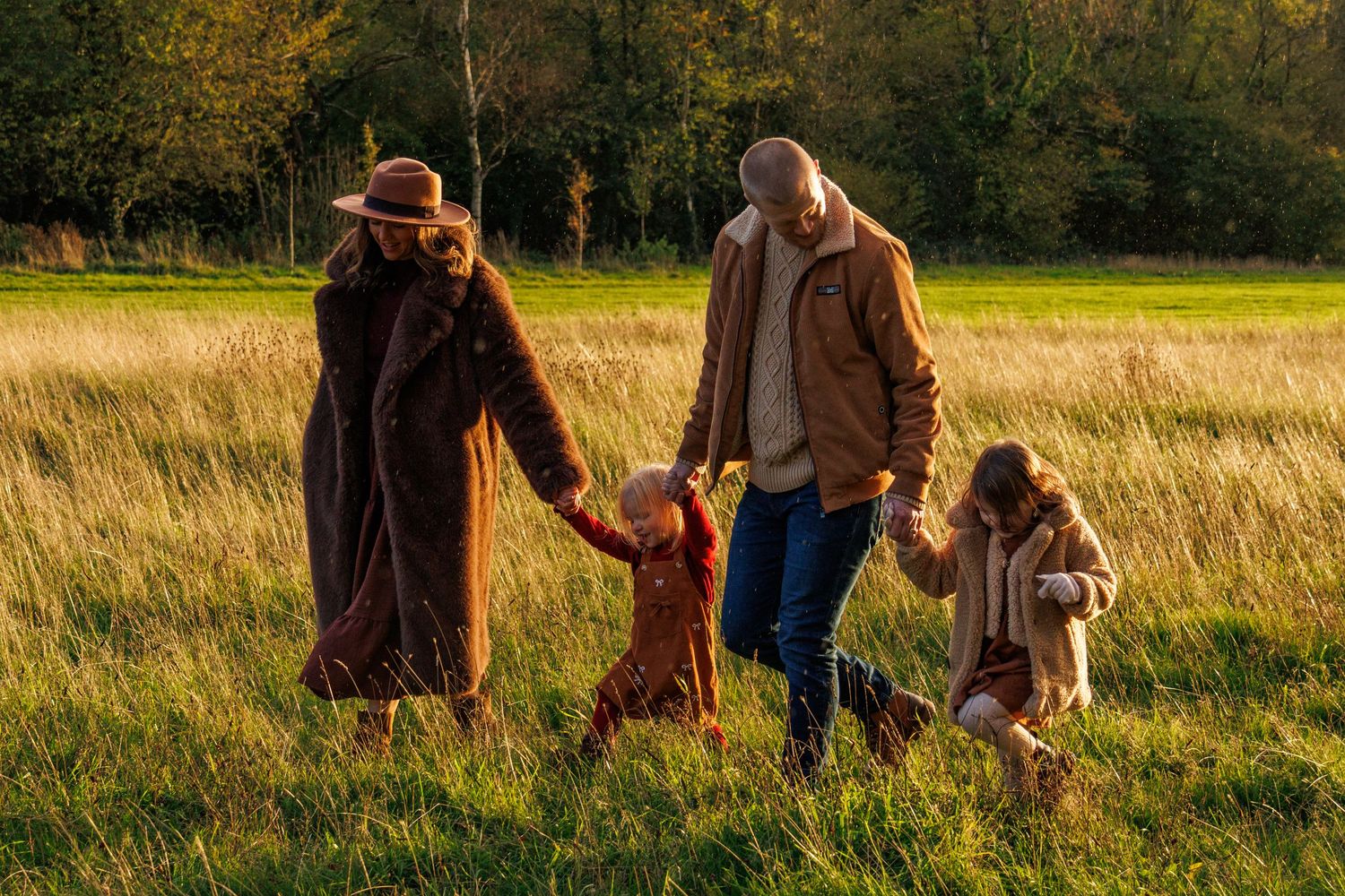 Family walking together through a golden autumn field at sunset in warm coats and winter clothing.