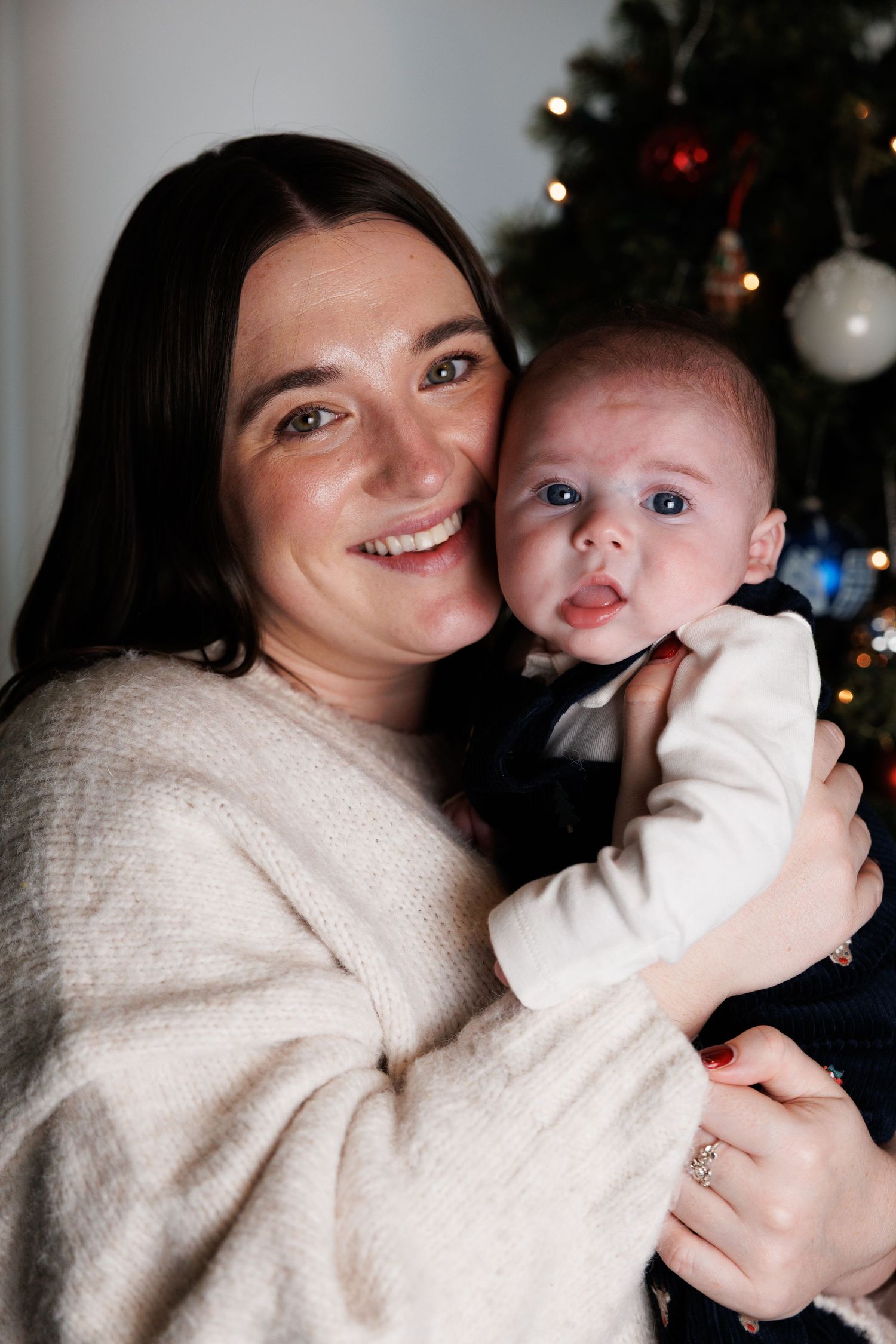 A heartwarming series of candid moments showing tender embraces between parent and baby against a Christmas tree backdrop.