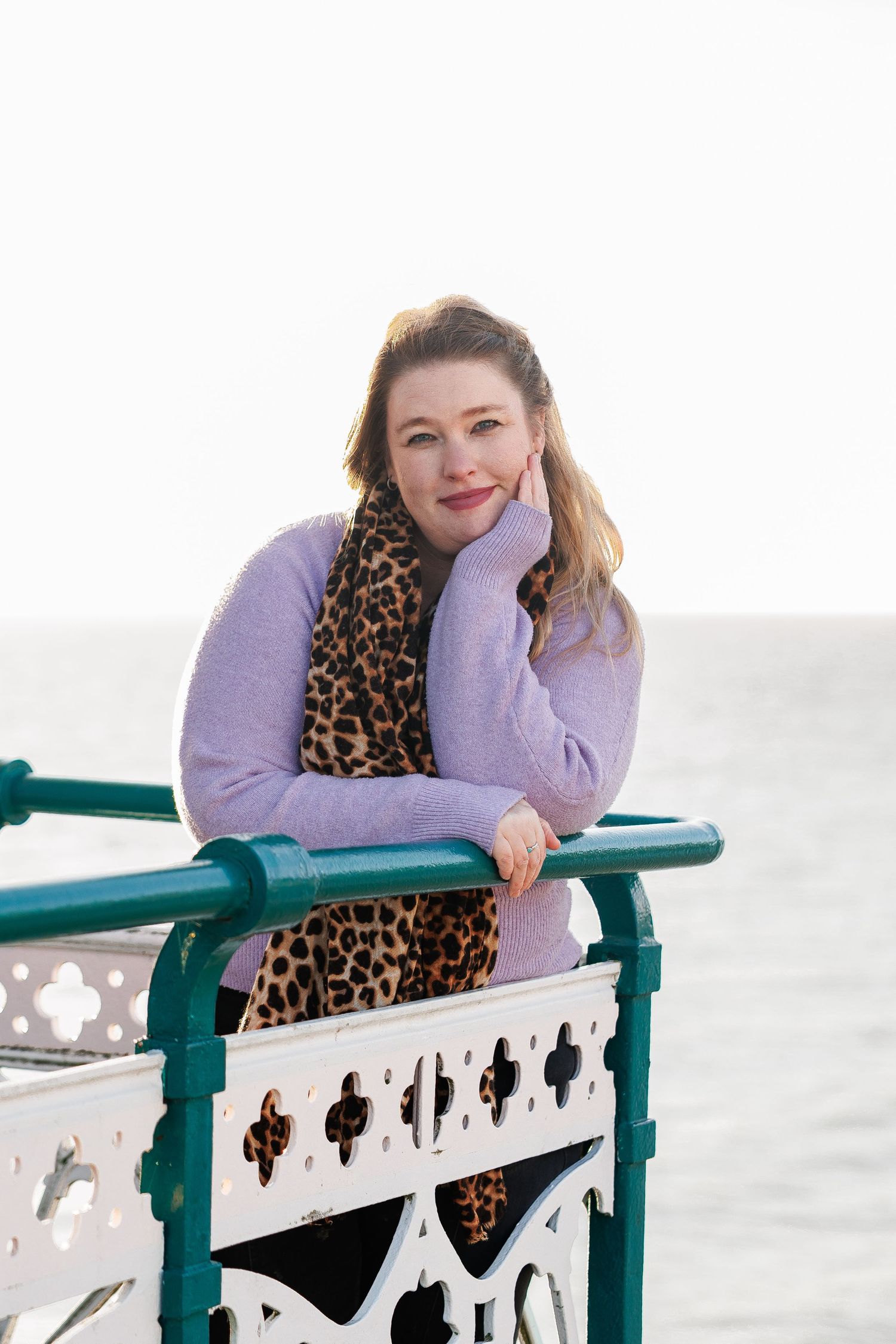 Person in a purple sweater and leopard print scarf poses along a white railing with decorative cutouts.