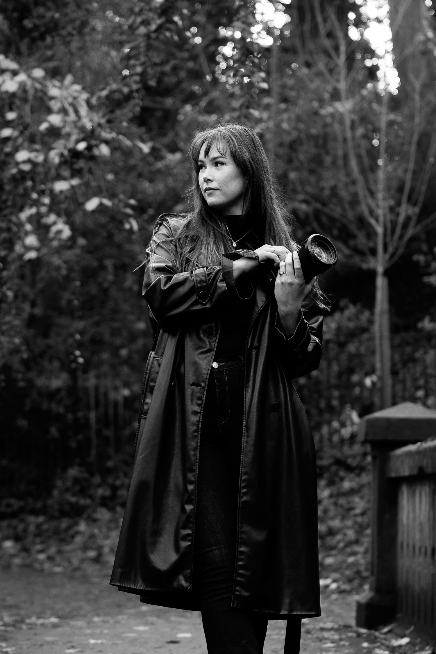 A person in a black coat stands in a wooded area creating a dramatic silhouette against the trees in the background.