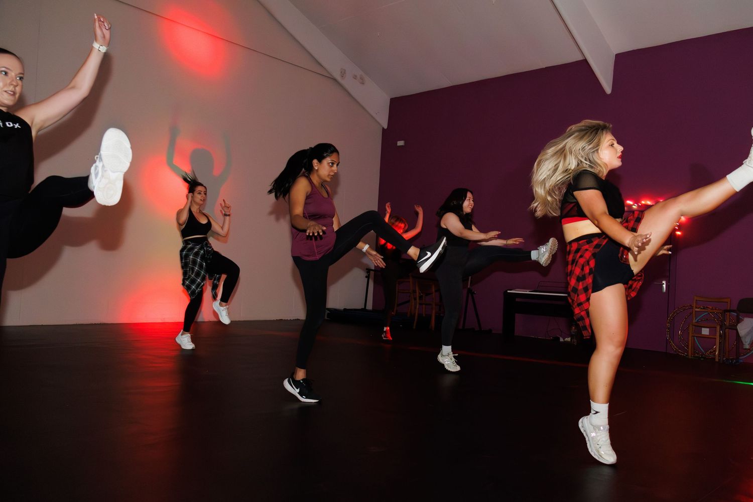A sequence of dance moves showing a person jumping and kicking in a purple-lit dance studio.