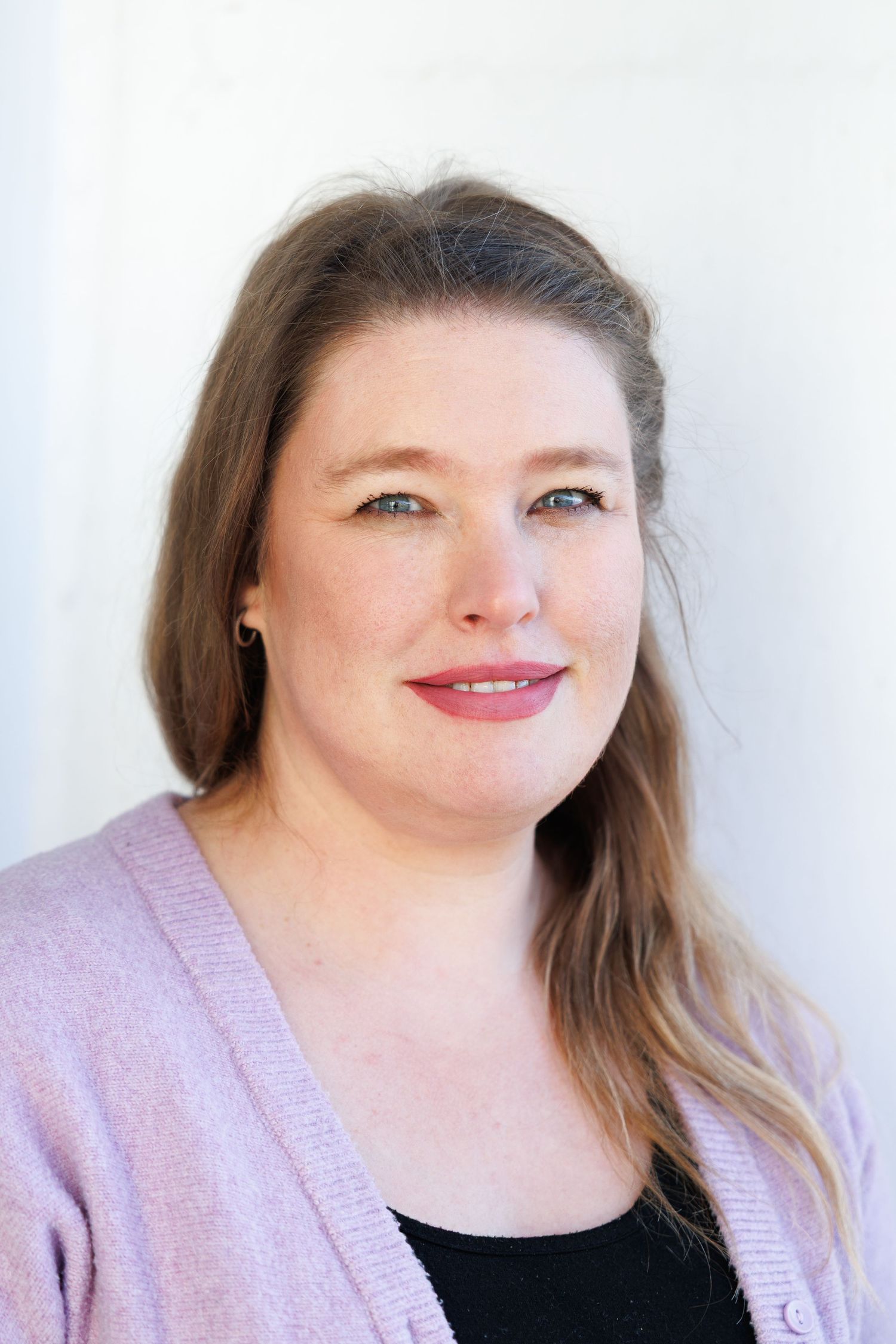 Professional headshot portrait of a person wearing a light purple cardigan over a black top against a white background.
