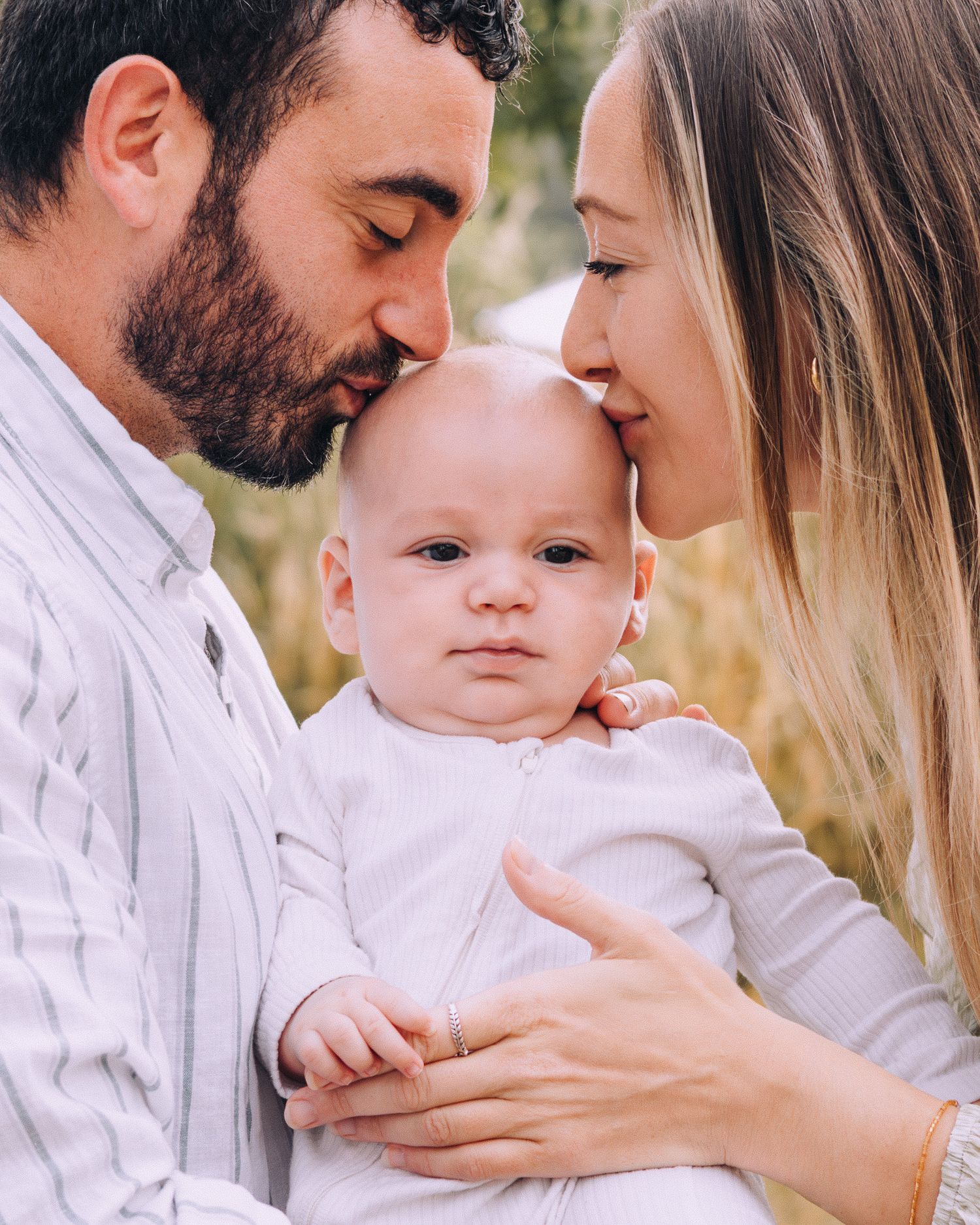 A series of intimate family portraits in white clothing showing tender moments with a baby outdoors.