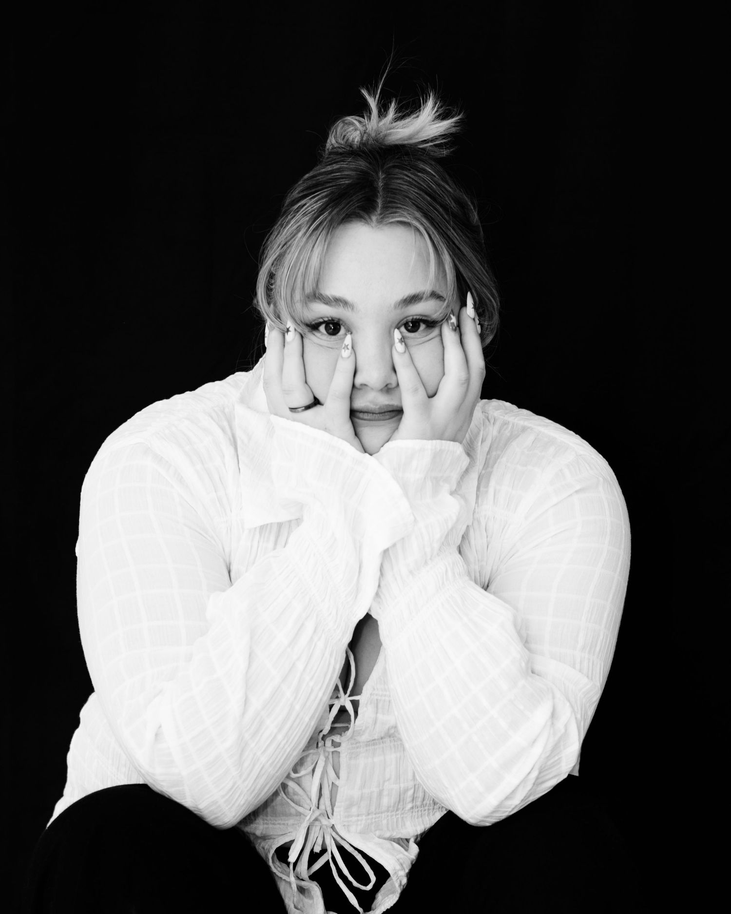 A black and white photo series showing someone in a white top posing with hands covering their face in different ways.