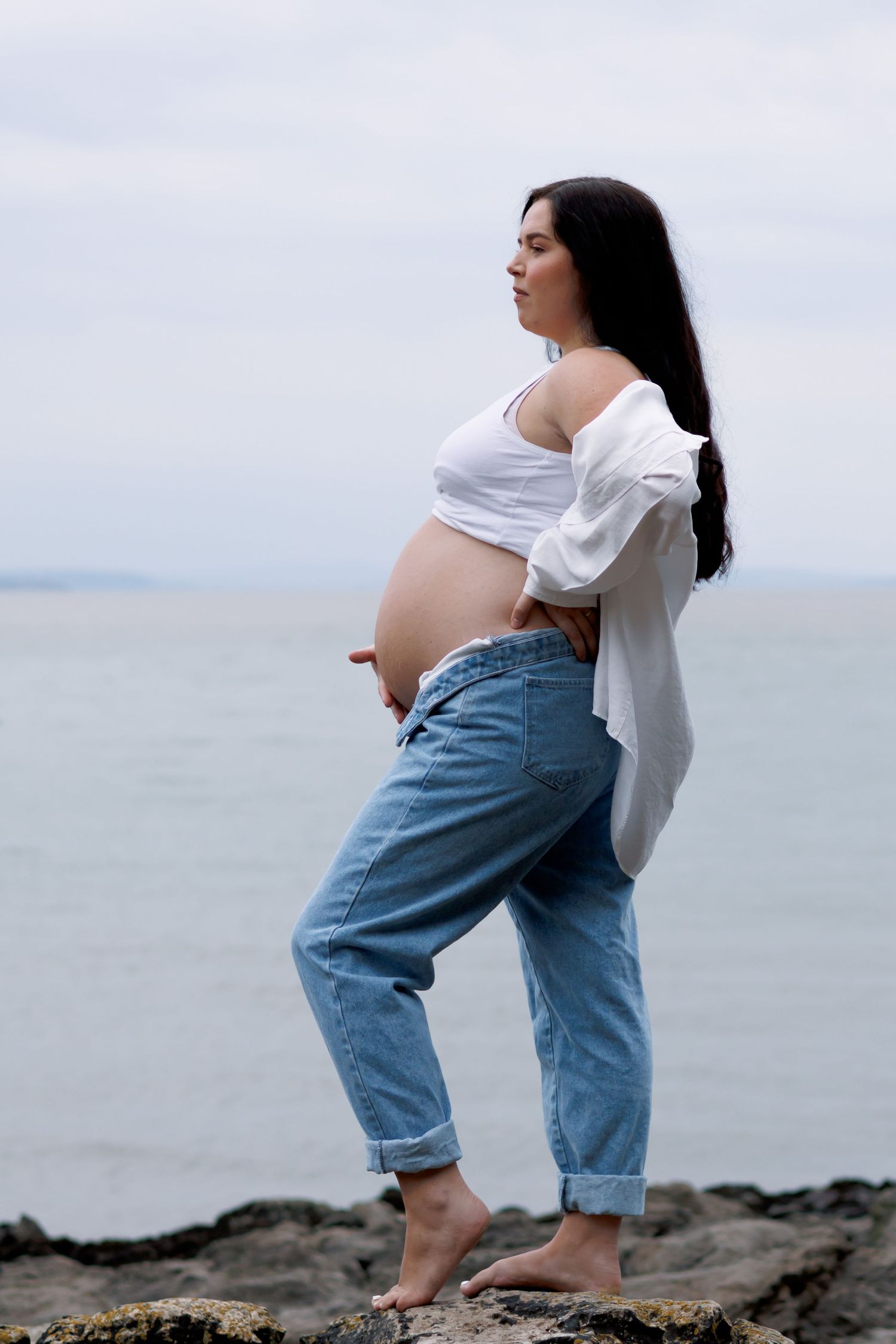 A row of beach maternity photos showing a woman in a white shirt and jeans posing by the ocean.