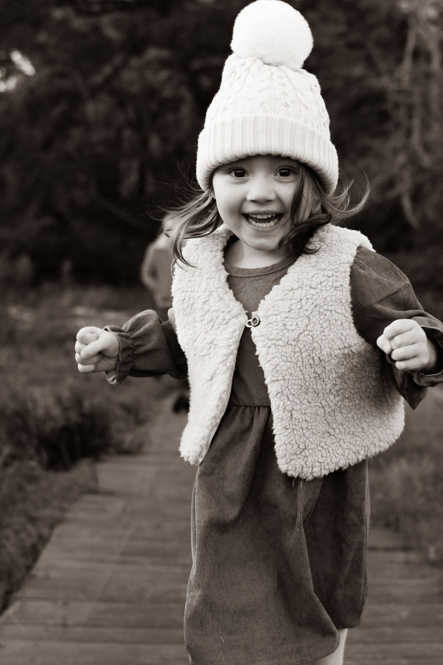 A child in a white winter hat and brown coat poses playfully in a series of black and white photos.