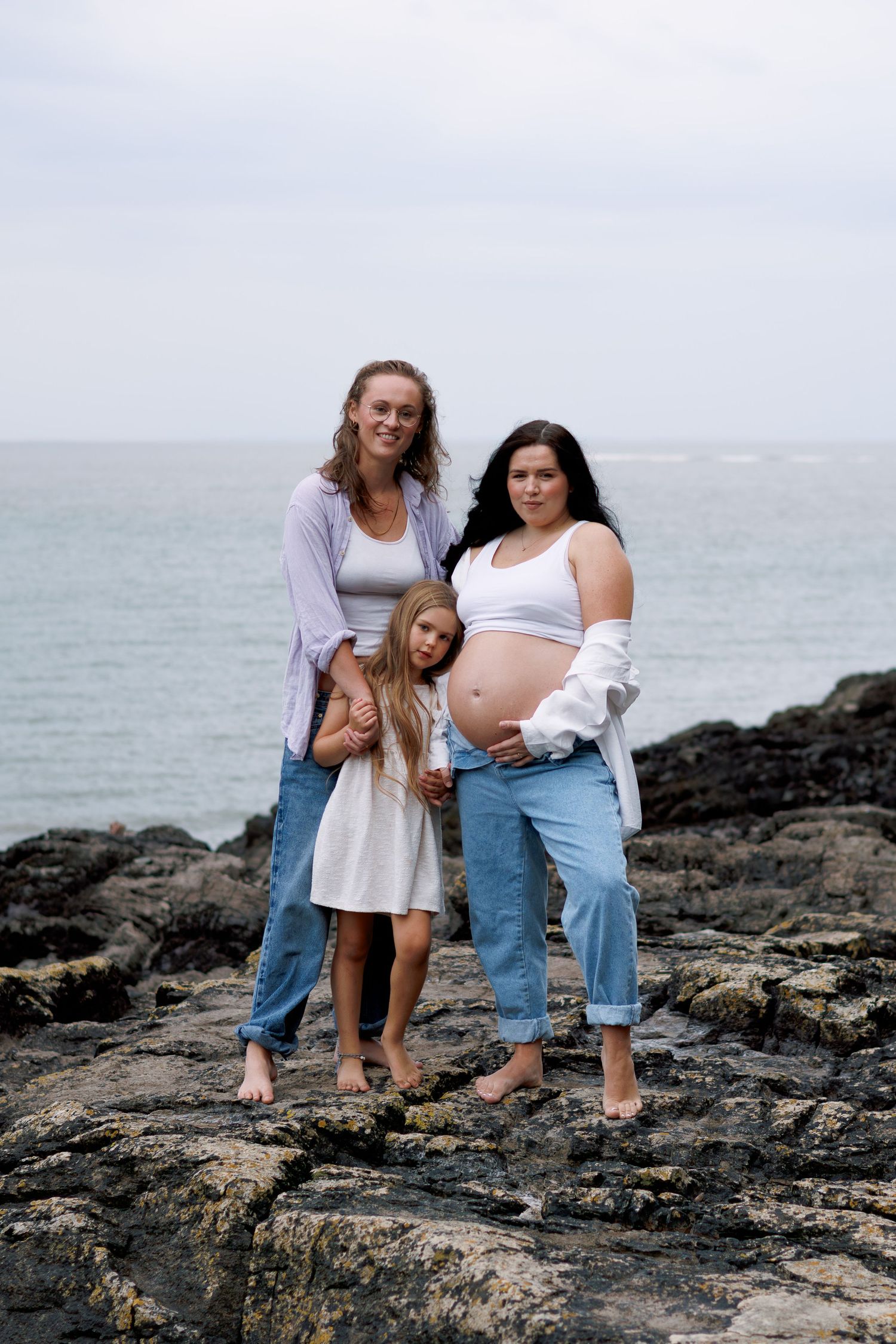 Three progressive photos show a family posing together on rocky coastal terrain with ocean waves in the background.