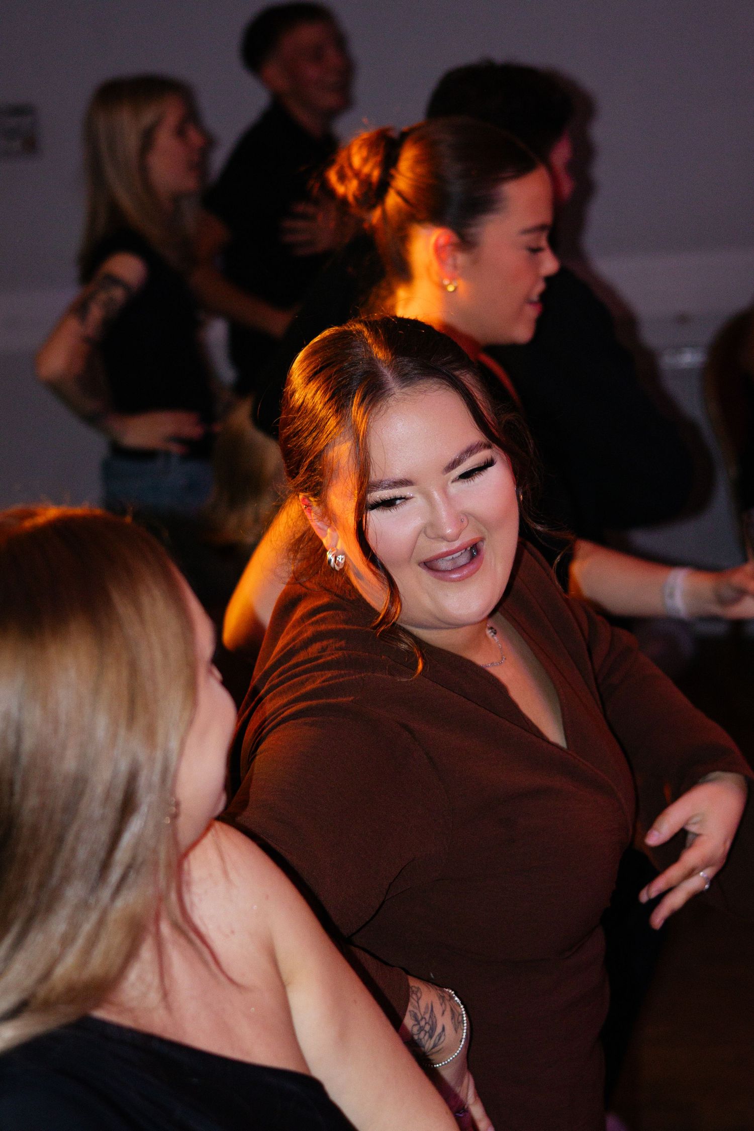 Two people share a joyful moment while dancing together in a dimly lit room with warm lighting.