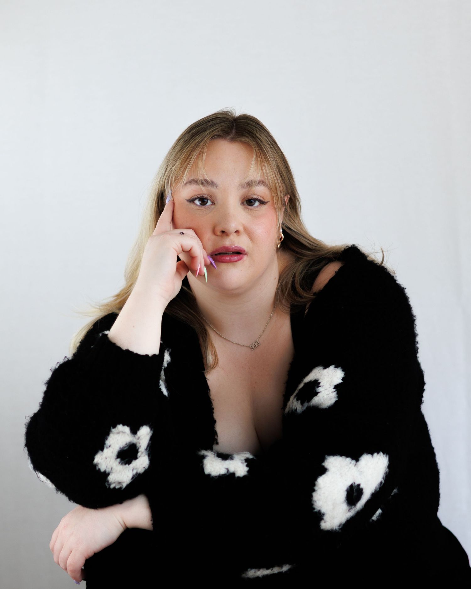 A person in a black fuzzy sweater with white floral details poses playfully against a light background.