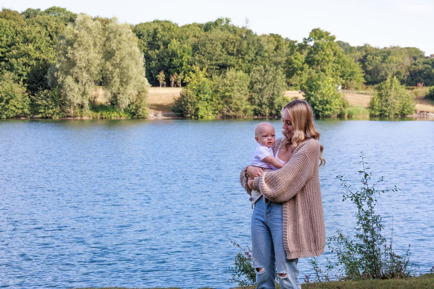Group enjoying summer afternoon by scenic lake surrounded by lush green trees and natural landscape.