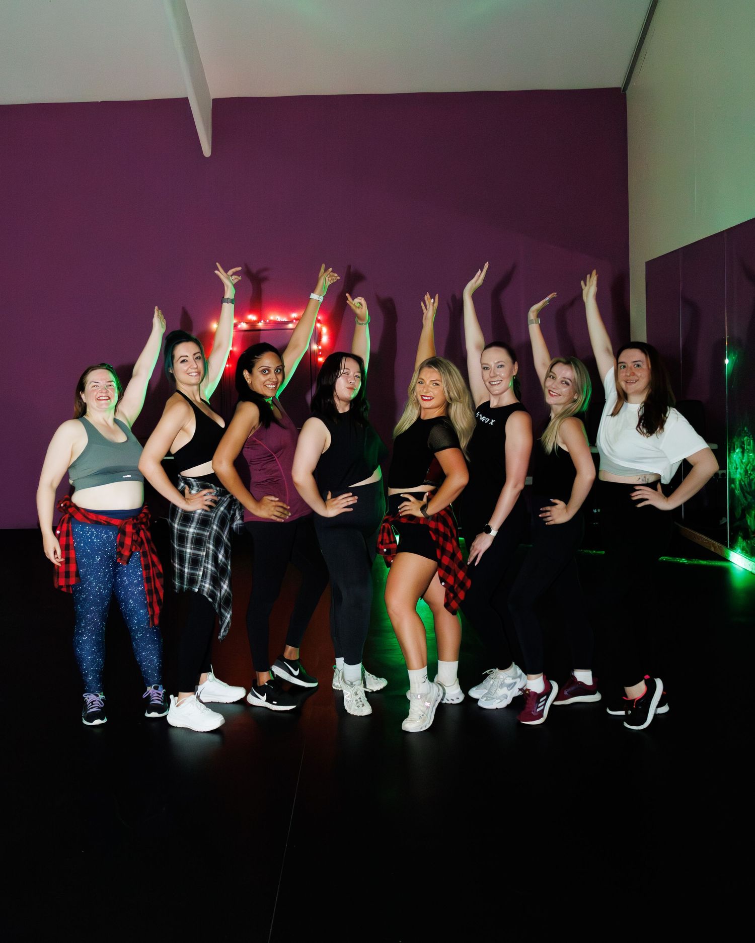 A group of dancers perform synchronized dance moves in a dimly lit room with colorful lighting effects.
