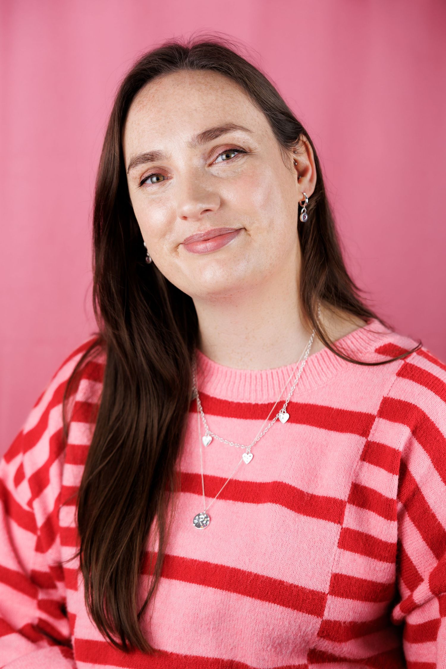 A person in a pink and red striped sweater poses against a pink background in a series of playful expressions.