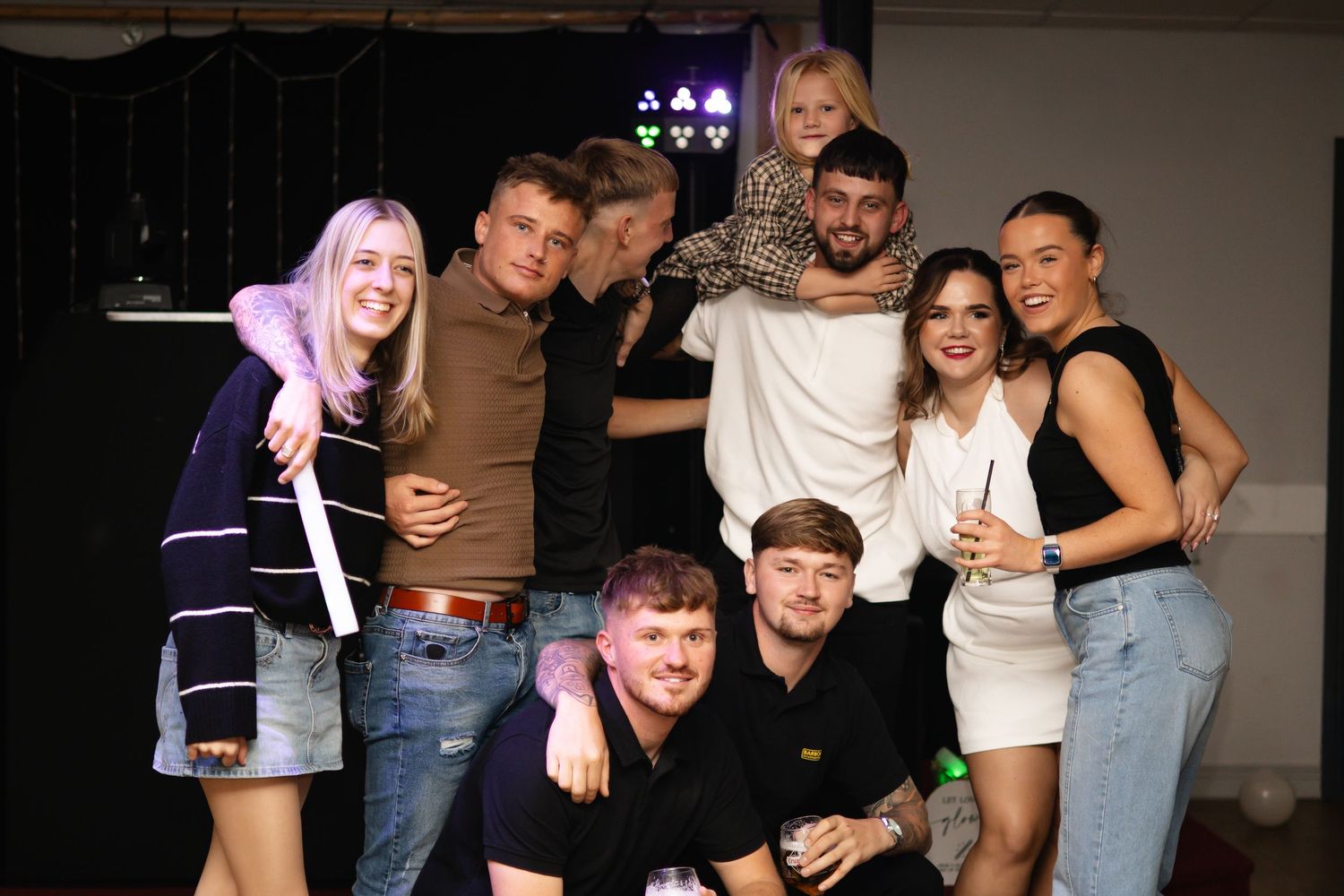 A group of friends posing together at a party in casual outfits with jeans and t-shirts.