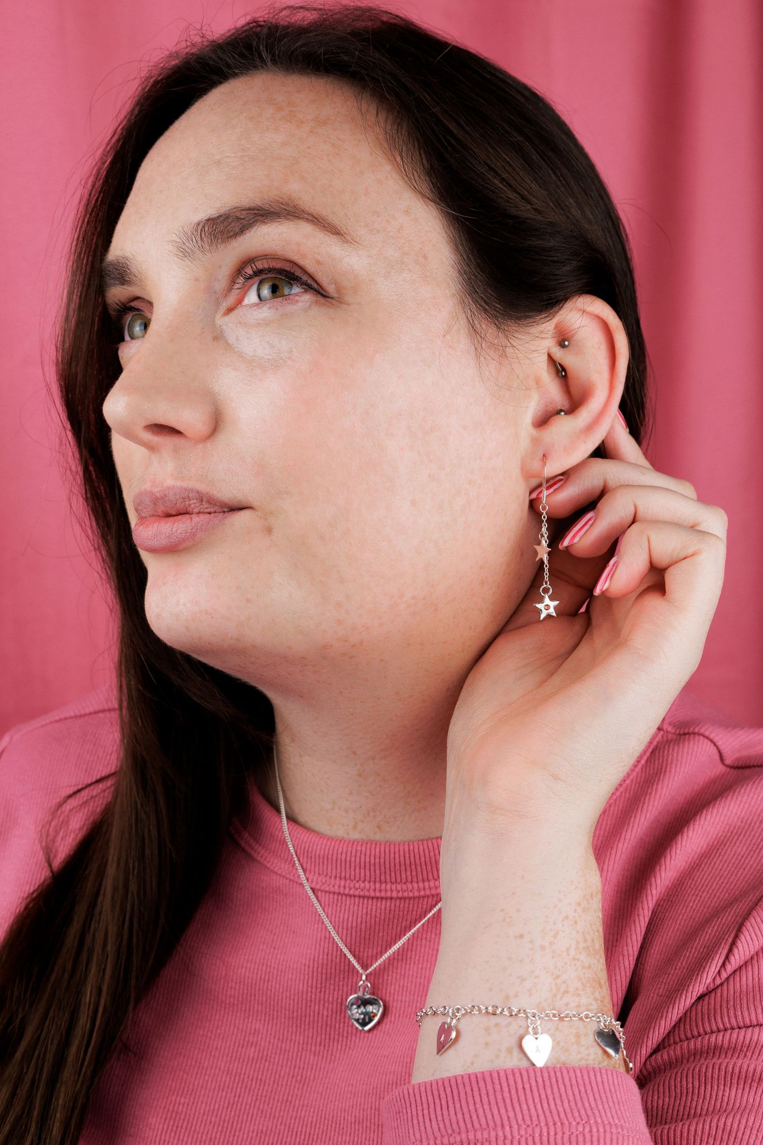 Close-up sequence showing someone putting on a delicate silver necklace against a pink background.