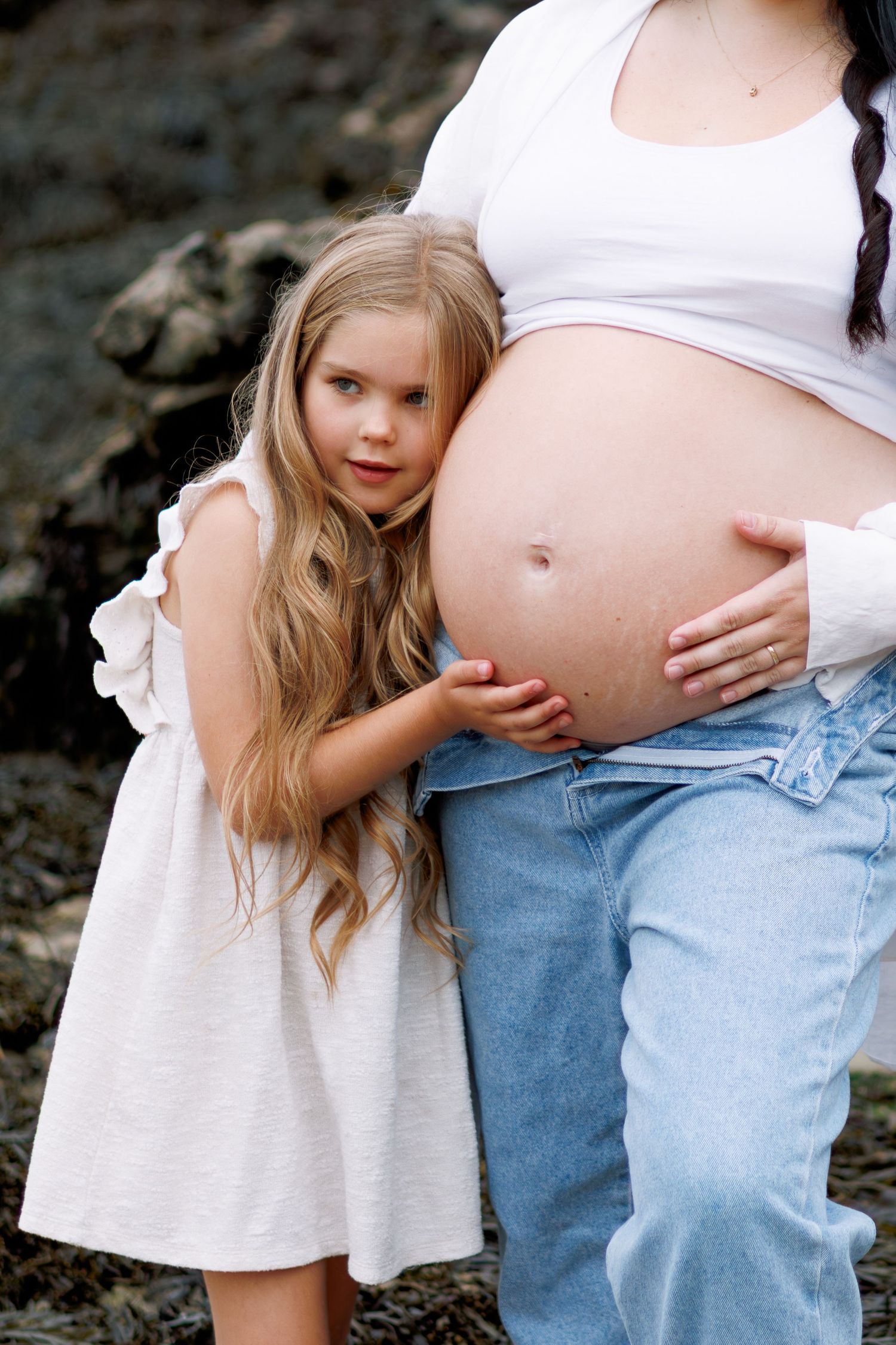 A series of tender moments showing a child in a white dress gently touching a pregnant belly in light denim jeans.