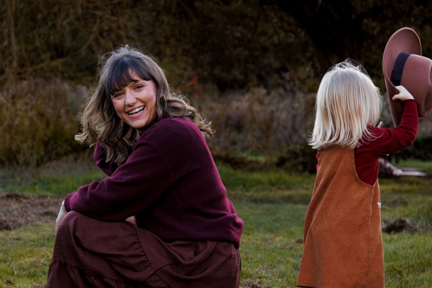 A group of people sit together on a wooden bench in an outdoor setting during autumn.