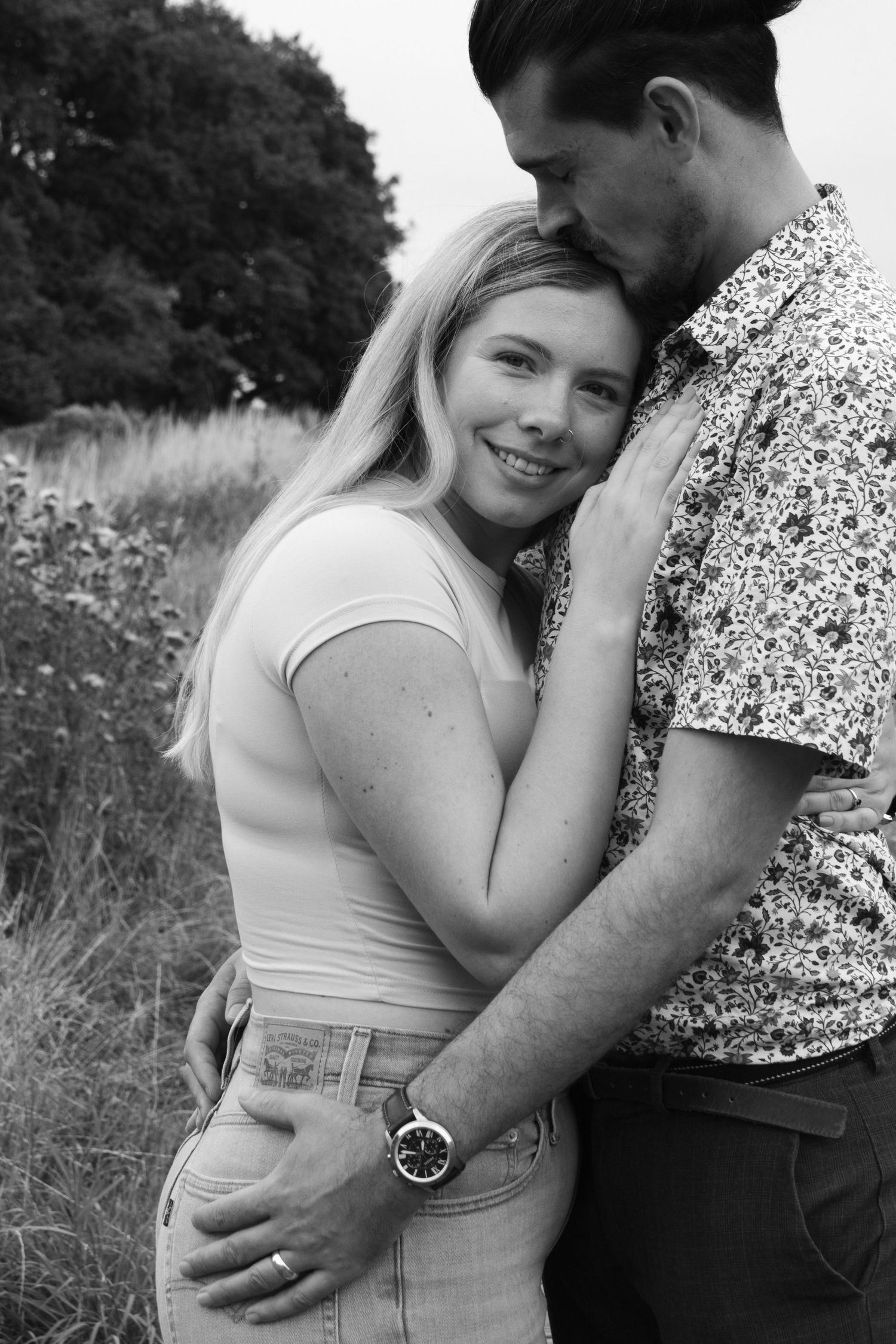 A romantic black and white photo series showing a couple embracing in an outdoor field setting.