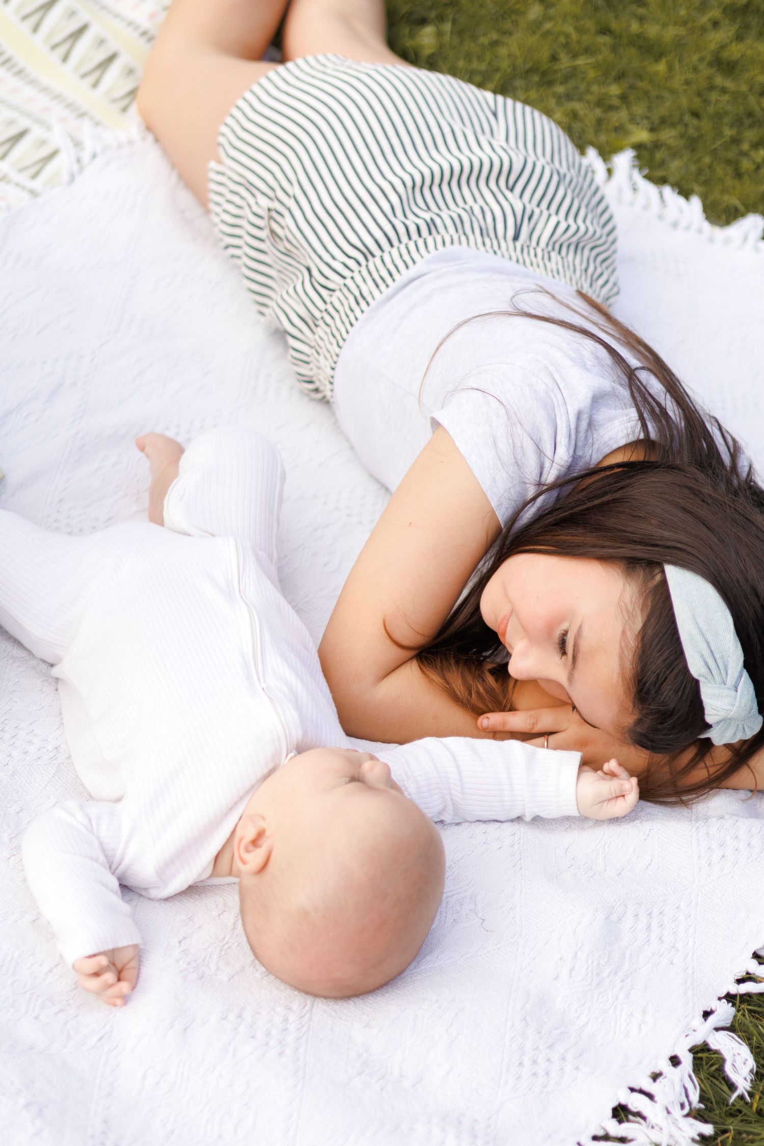 Person in white dress and striped shirt lying on white blanket on grass in outdoor setting.