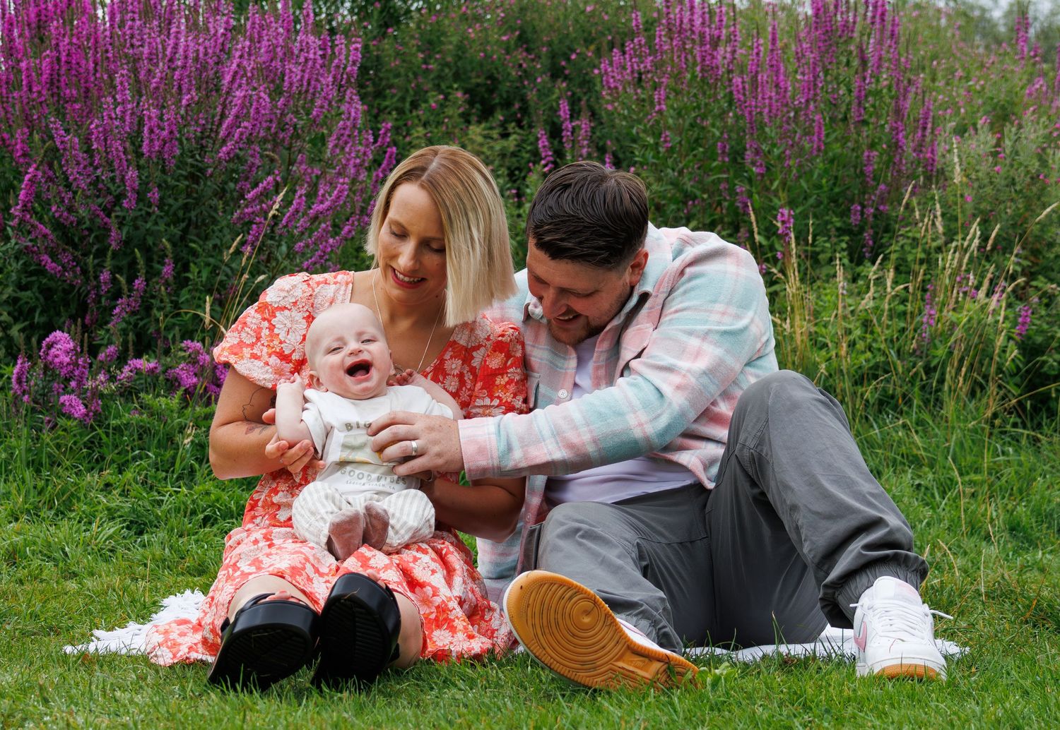 Family lying together on blanket in field of vibrant purple wildflowers during summer photo session.