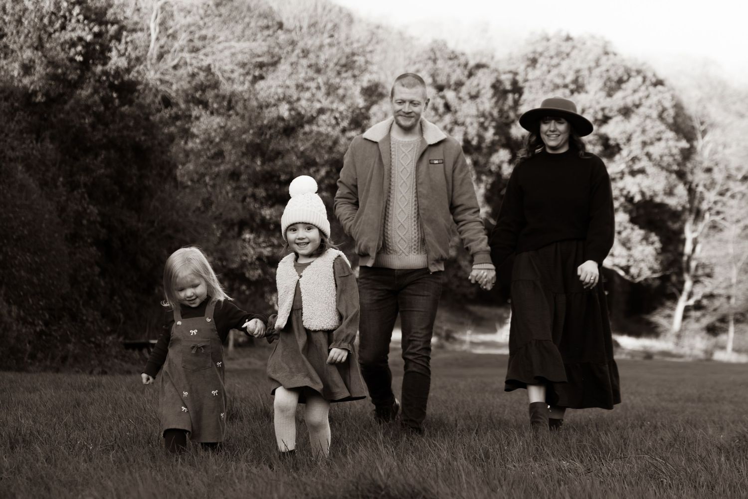 A vintage black and white photograph shows a family group walking together outdoors on a grassy path.