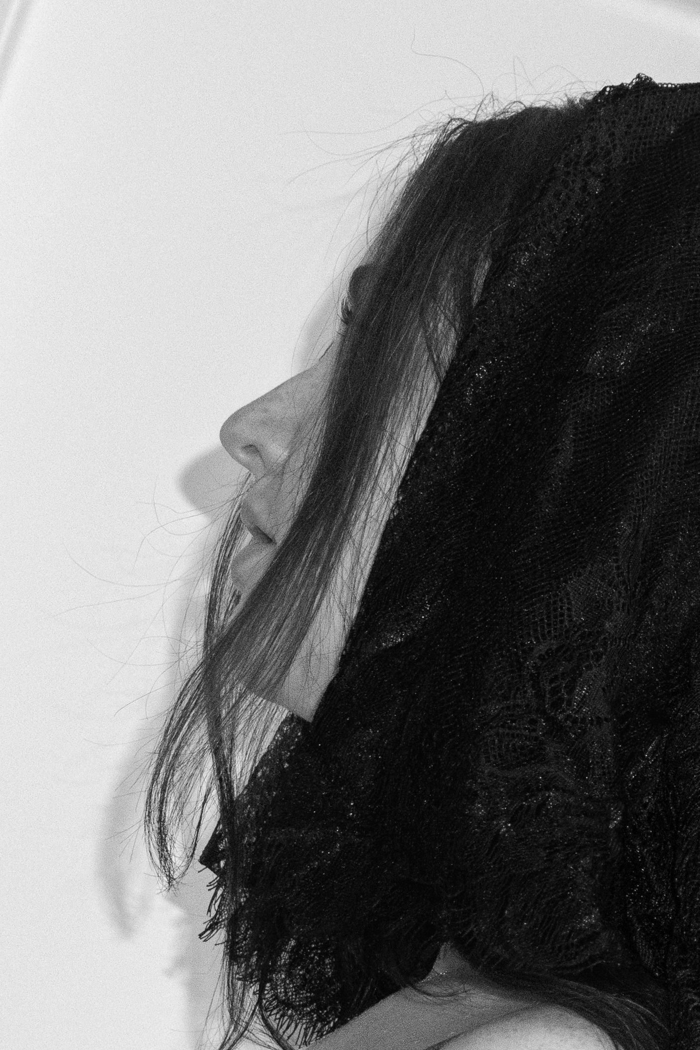 Black and white profile portrait of a woman with dark curly hair covered by a black lace veil.