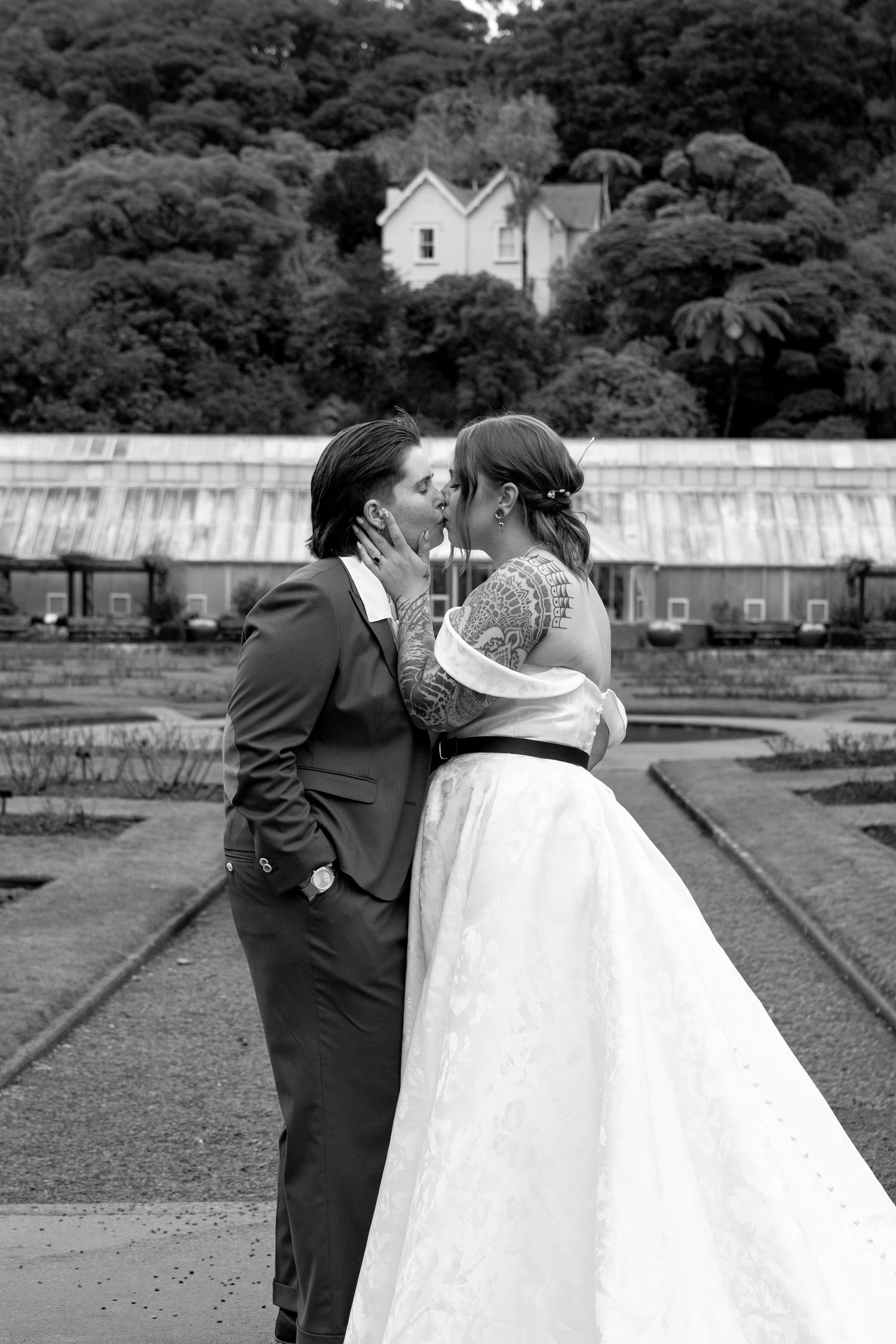 Black and white photo of a couple sharing a kiss on their wedding day in a formal garden setting.