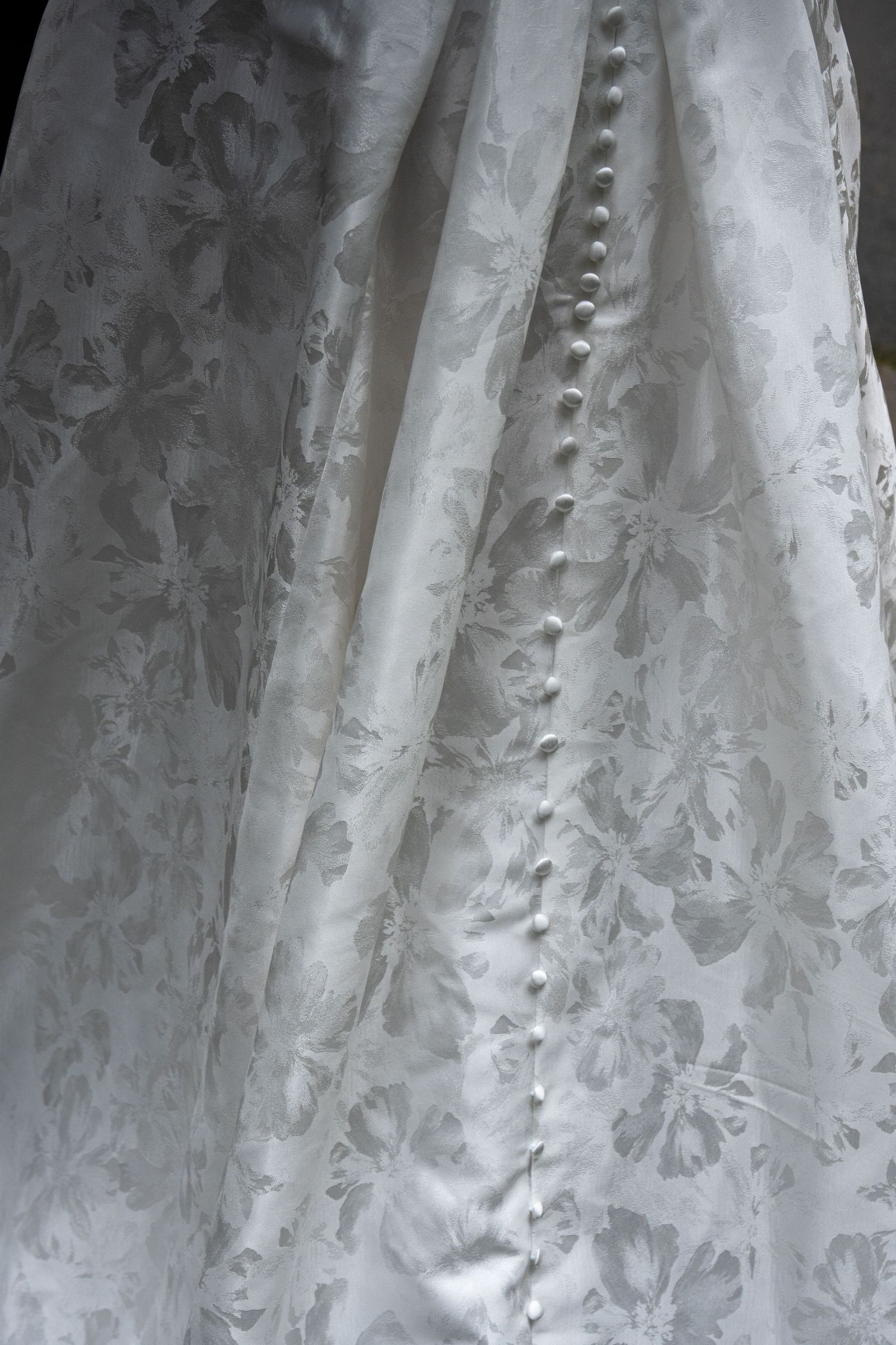 Close-up of elegant white floral damask wedding dress fabric with delicate pearl button closure detail.