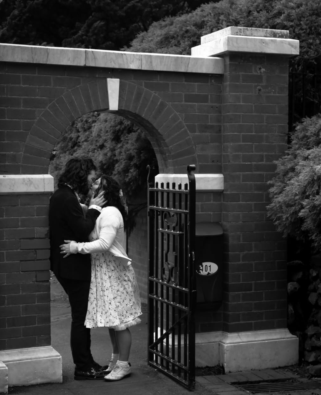 Black and white sequence showing couple interacting near a brick wall with iron gate.