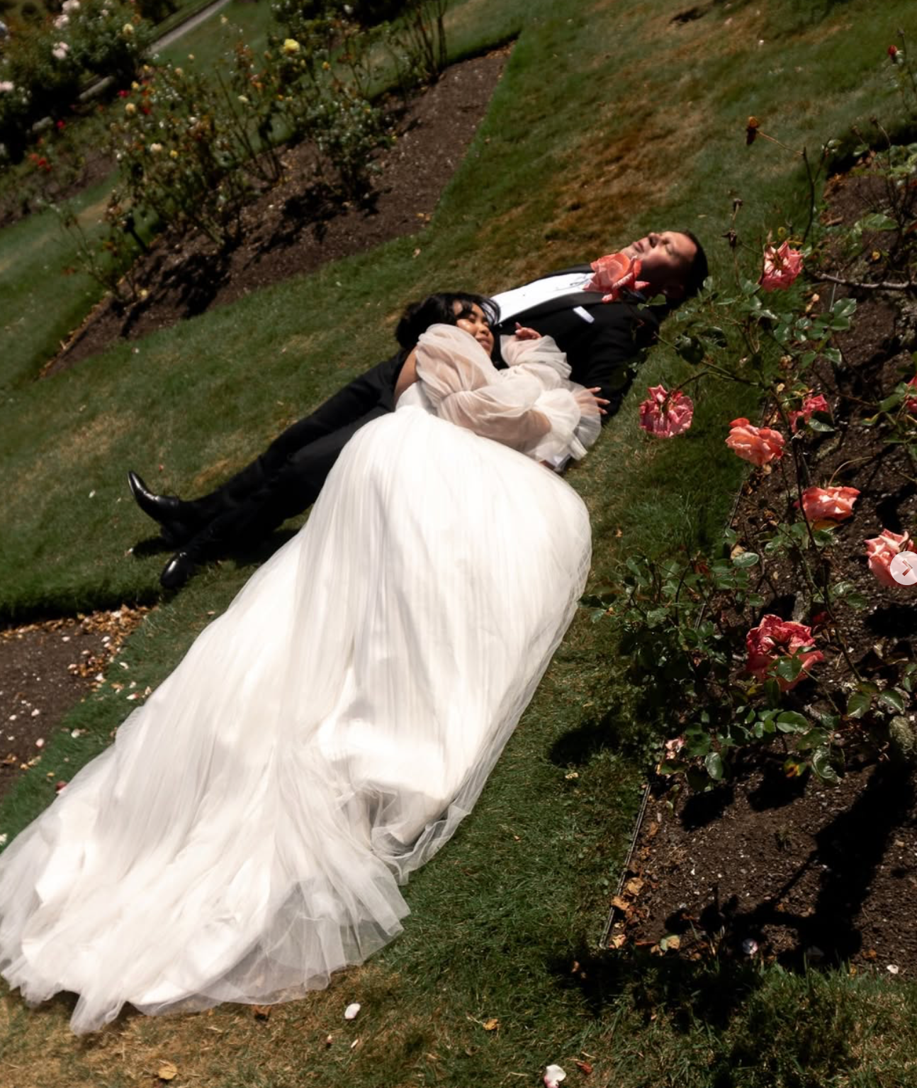 Wedding dress flowing on grass with pink flowers in garden setting.