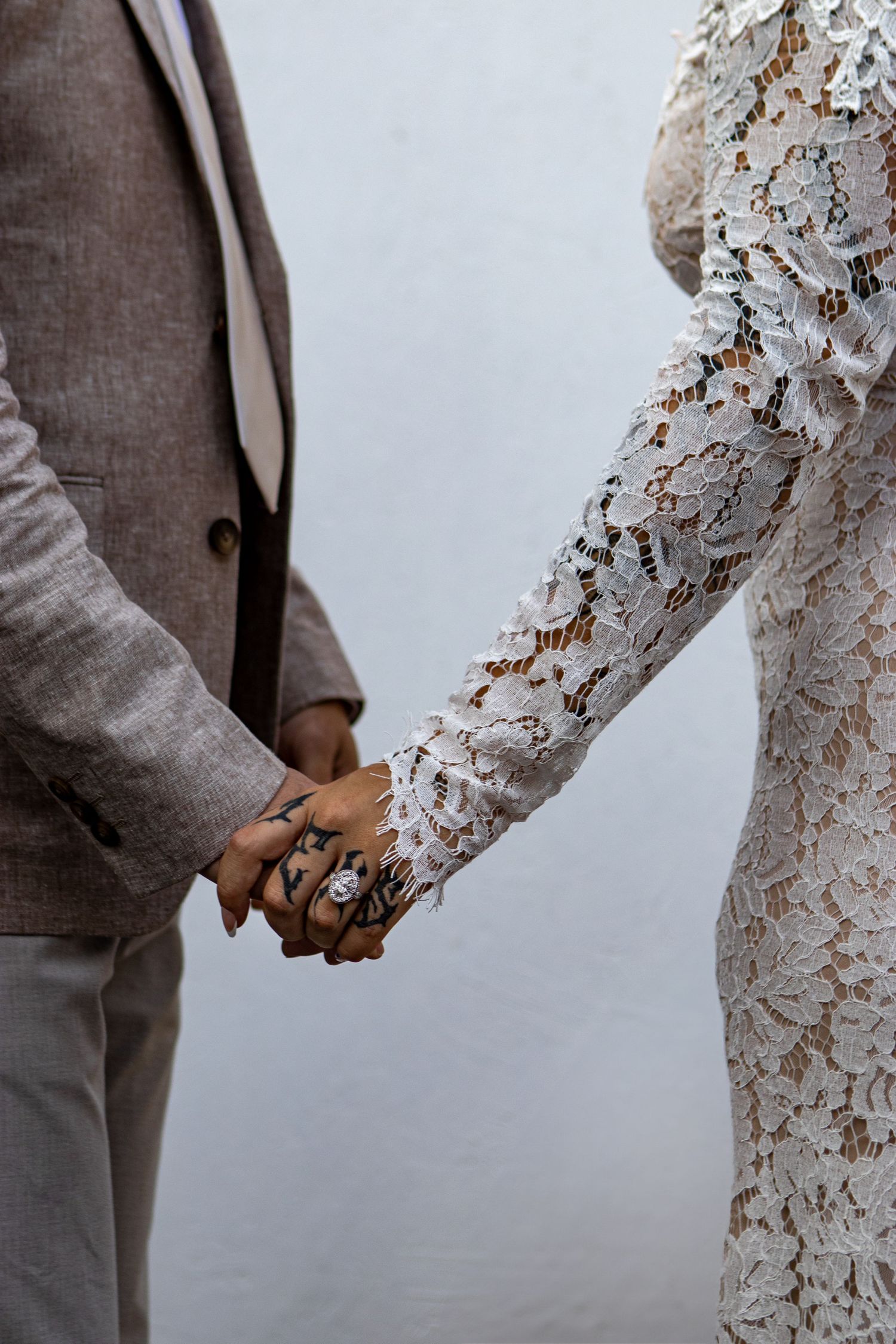 Close-up of couple holding hands, showing lace wedding dress sleeve and grey suit jacket.
