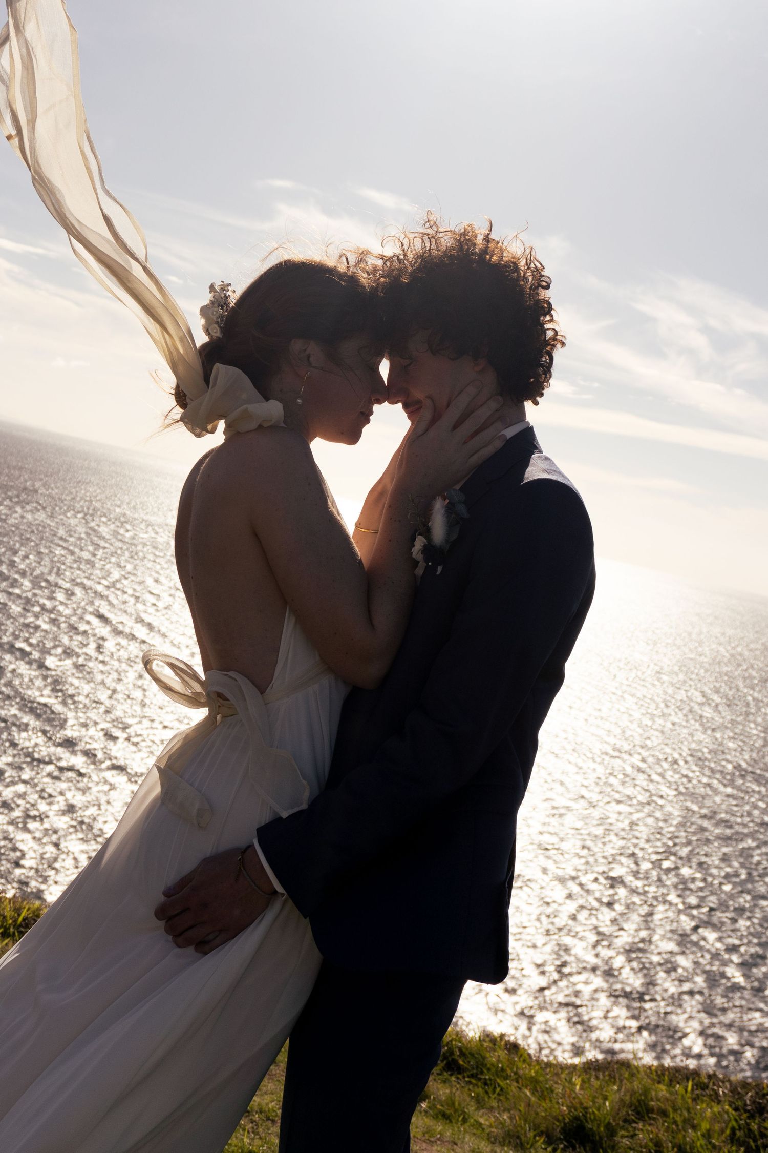 Silhouetted couple embracing on a cliff with dramatic ocean sunset in the background.