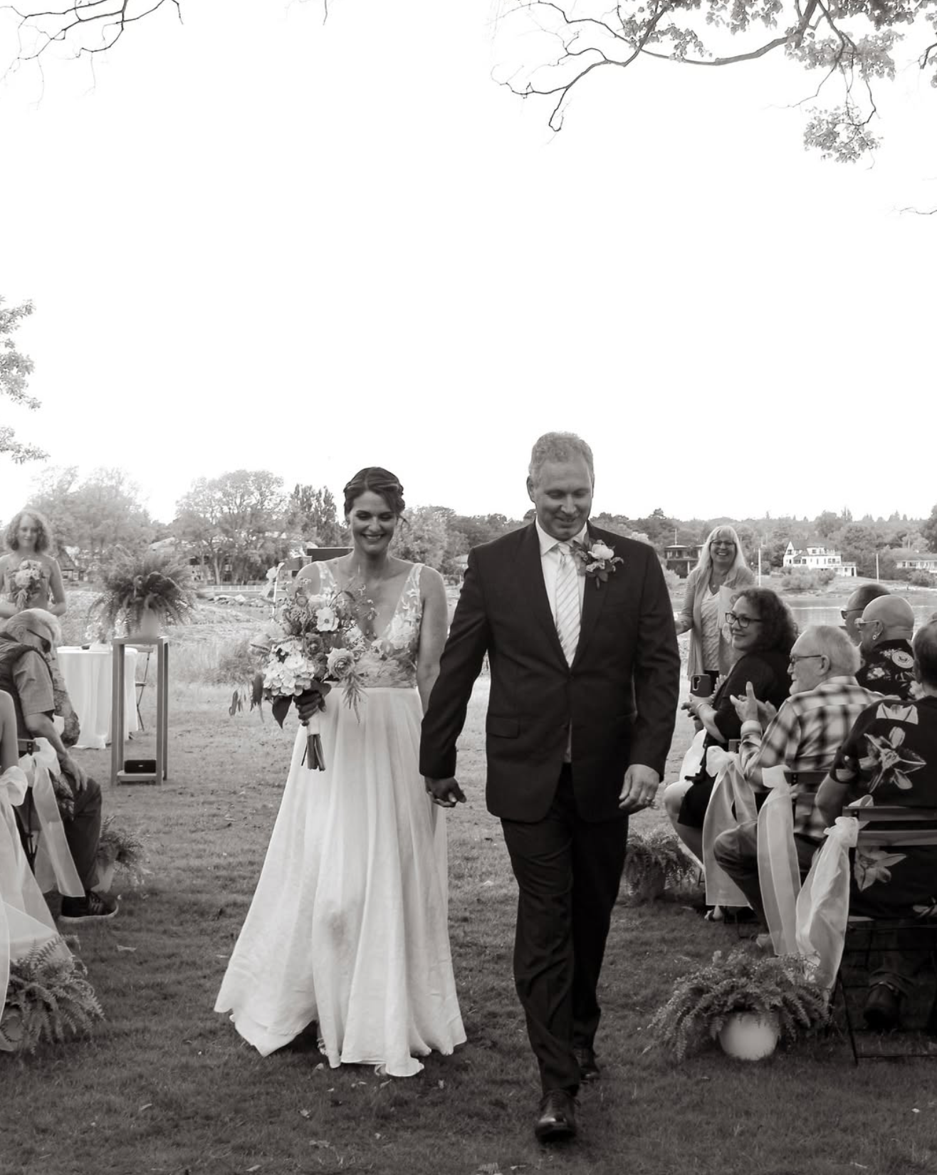 Black and white wedding ceremony processional showing couple and guests walking across an outdoor venue.