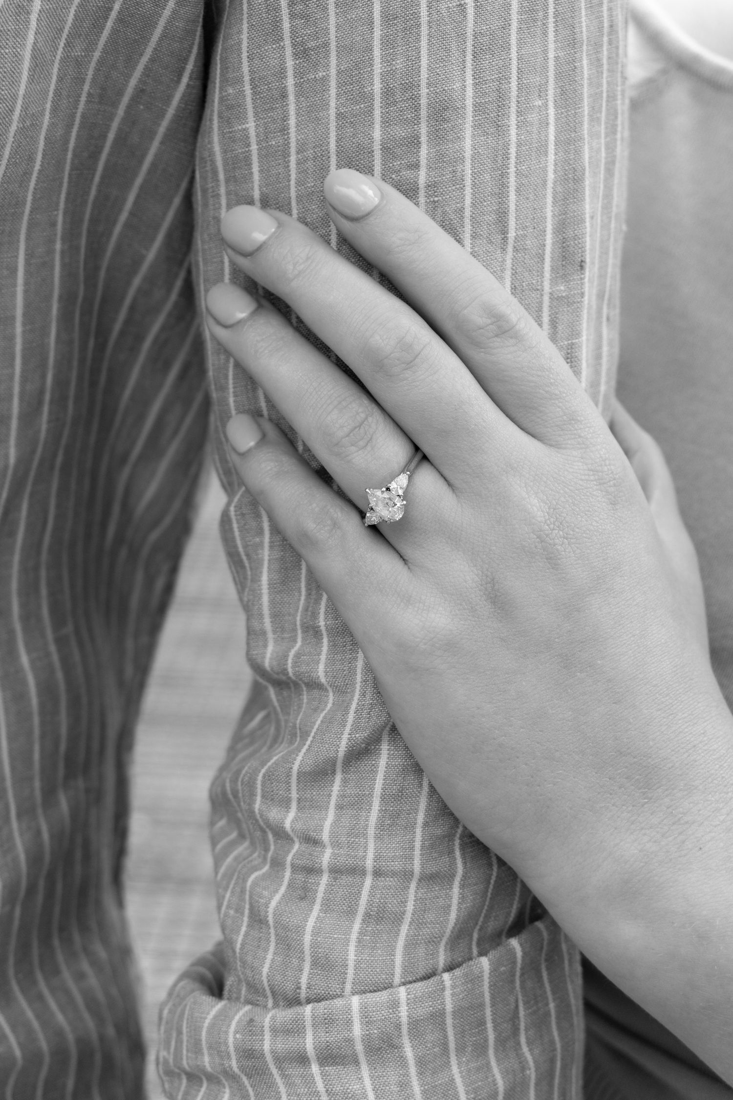 Black and white photo of a woman's hand wearing a diamond engagement ring, resting on a striped fabric.