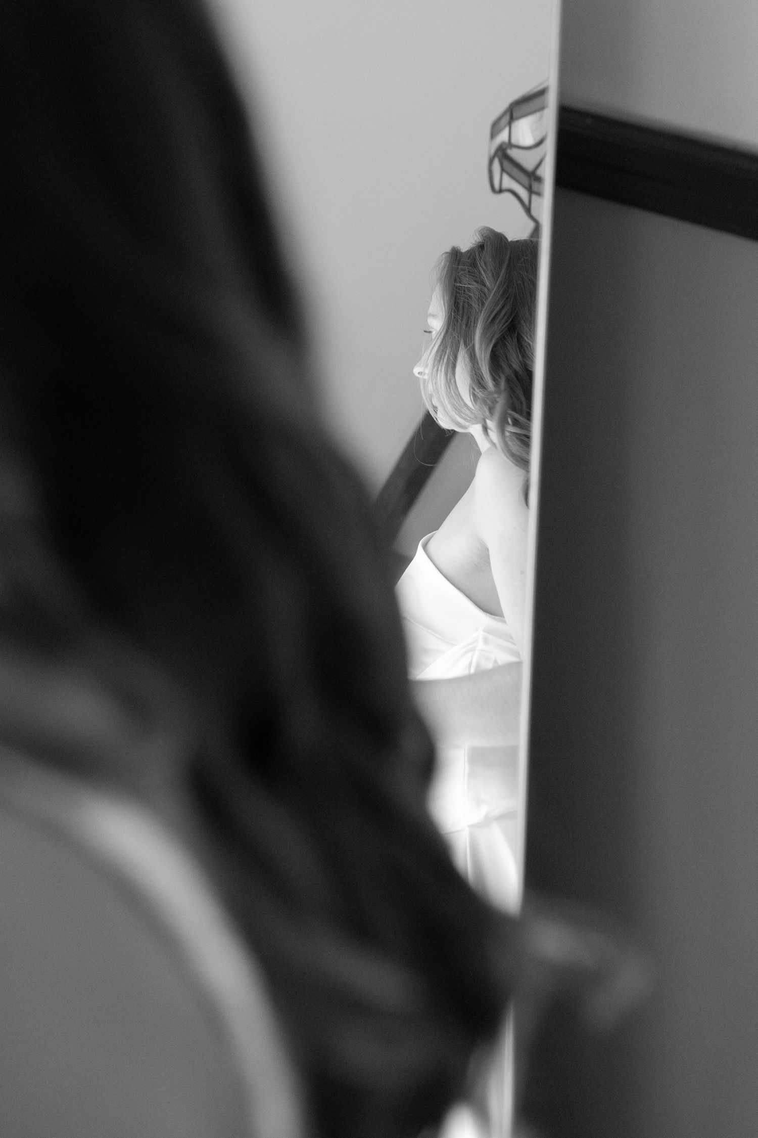 Black and white photo of a bride in white dress reflected in mirror with bridesmaid in foreground.