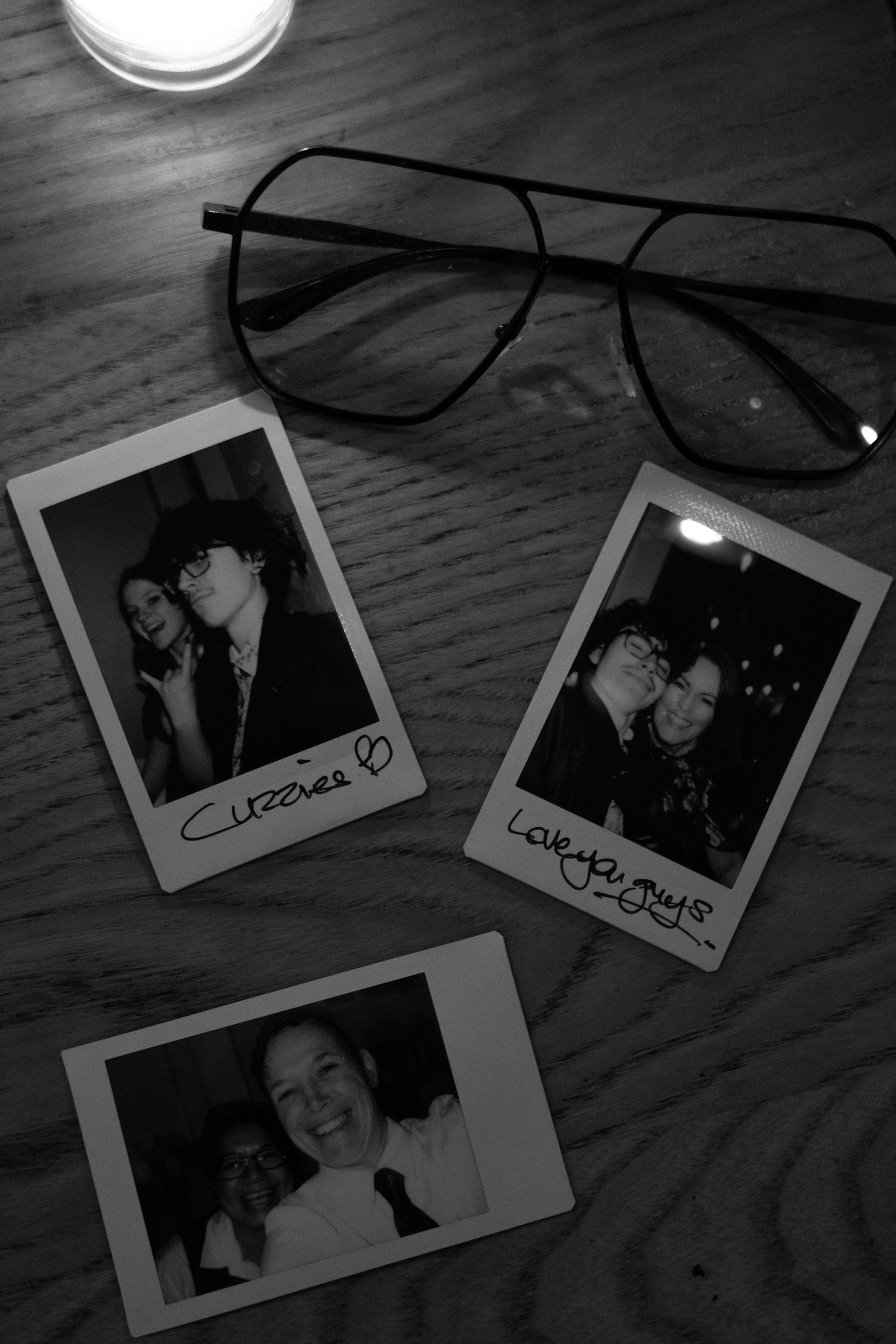 Vintage polaroid photos and glasses arranged on wooden surface in black and white.