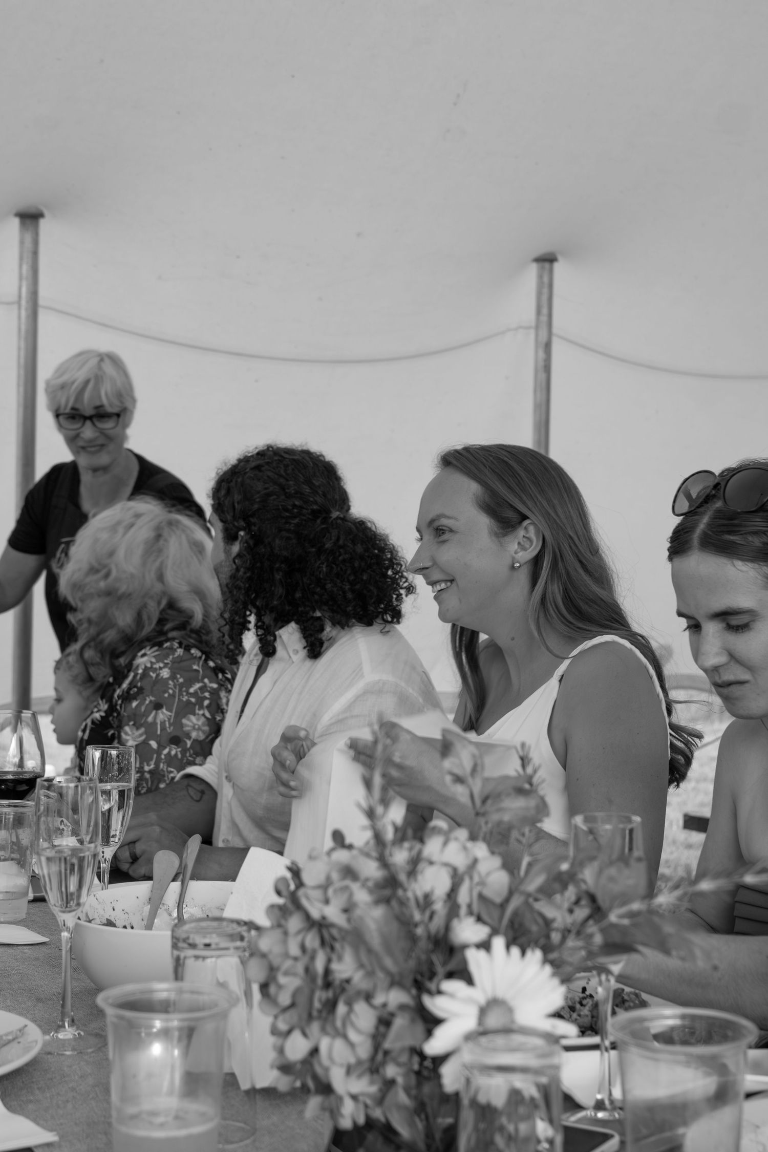 Black and white photo of women laughing and socializing at an outdoor garden party with floral centerpieces.