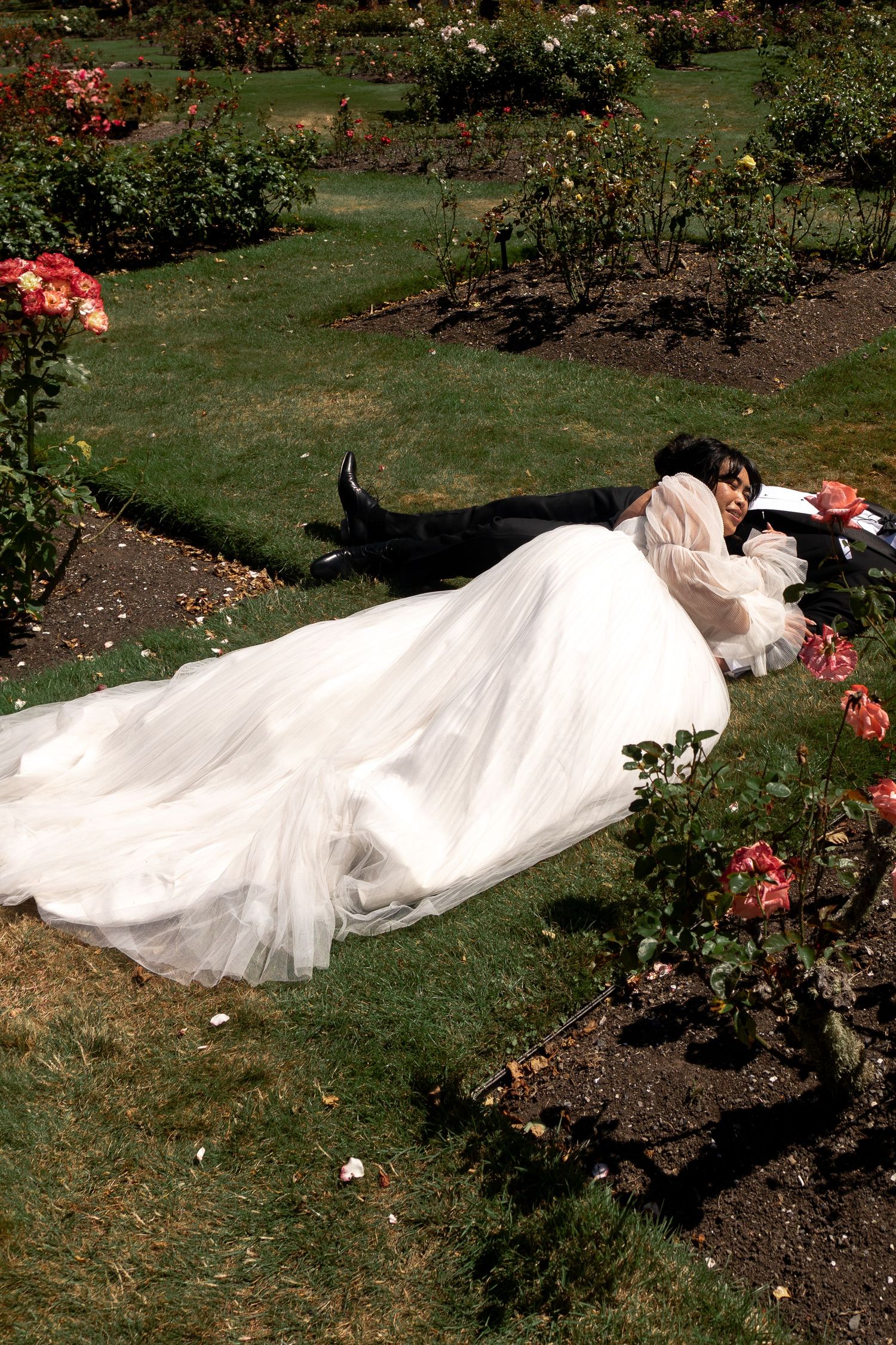 White wedding dress flowing on grass among rose bushes in a garden setting.