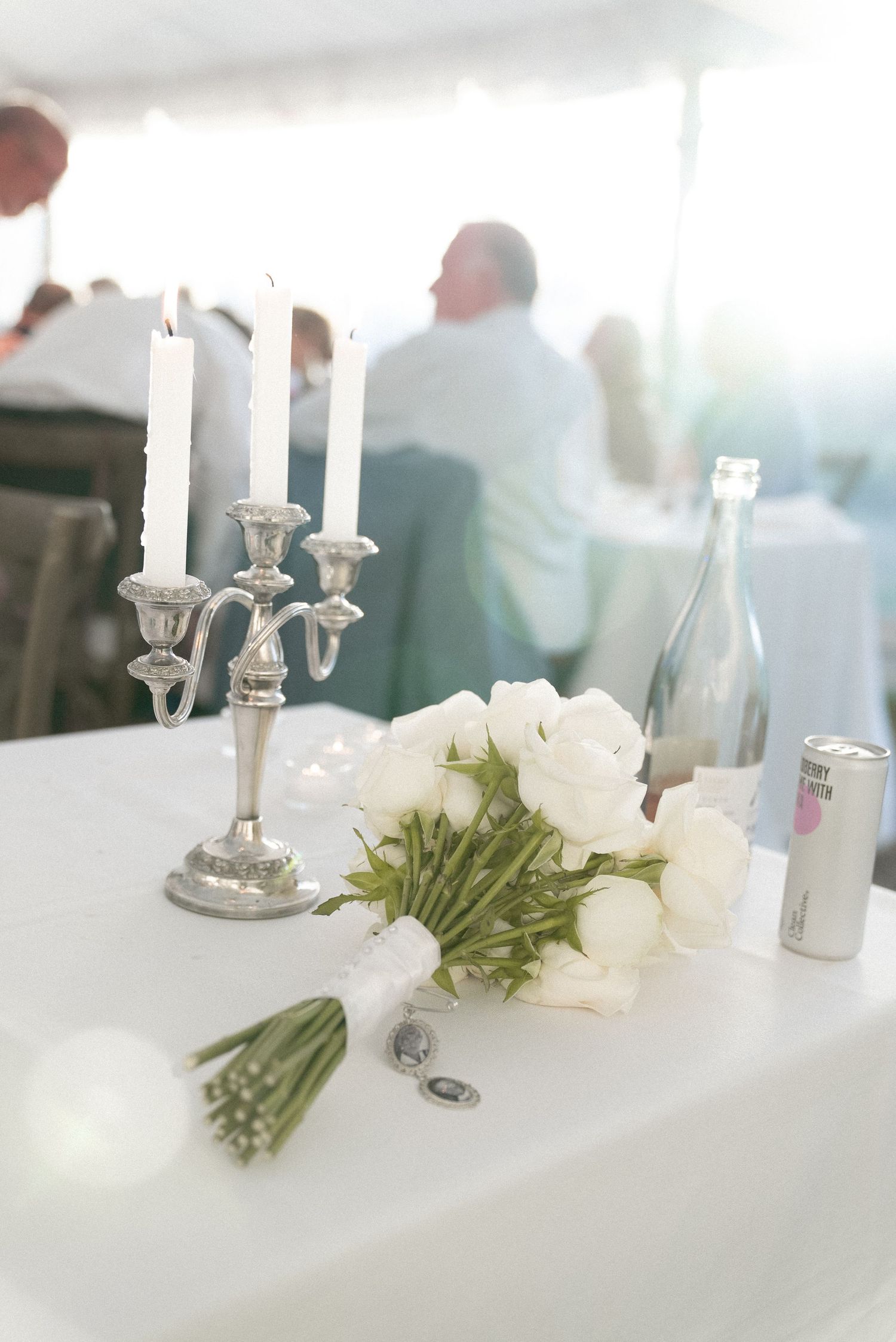 White ranunculus bridal bouquet on table with silver candelabra and bottle at elegant wedding reception.