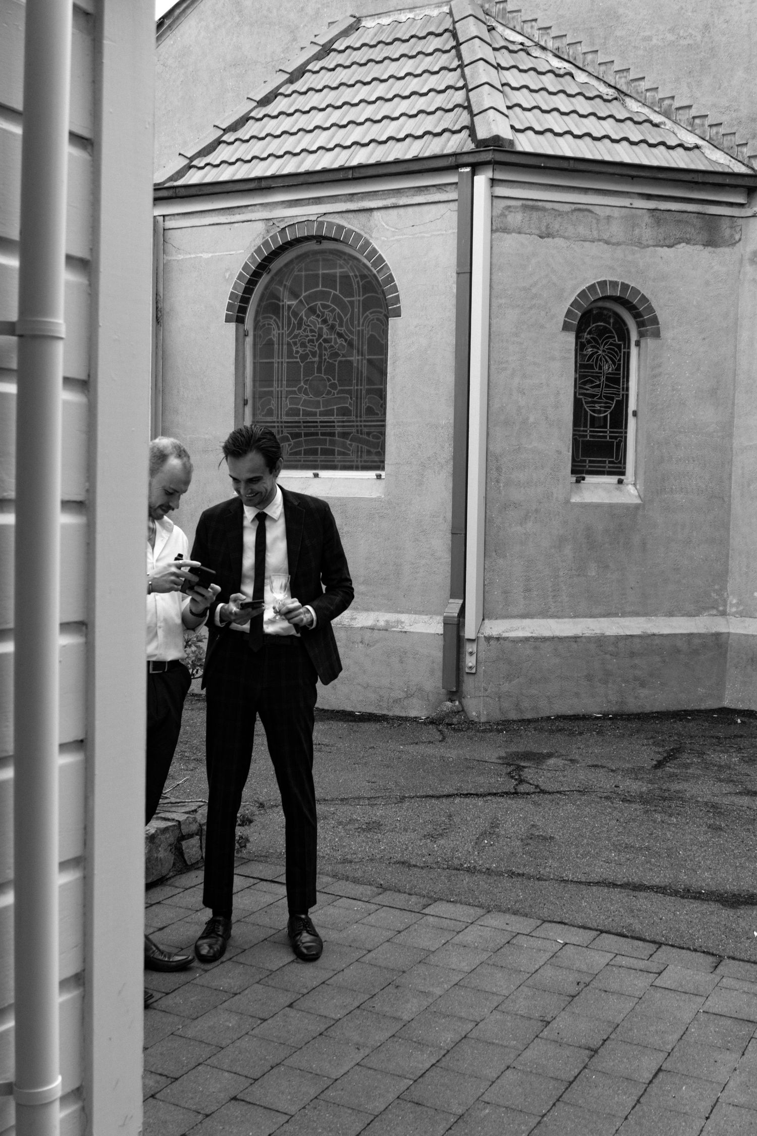 Black and white photo of two people in formal attire reviewing photos outside a historic church building.