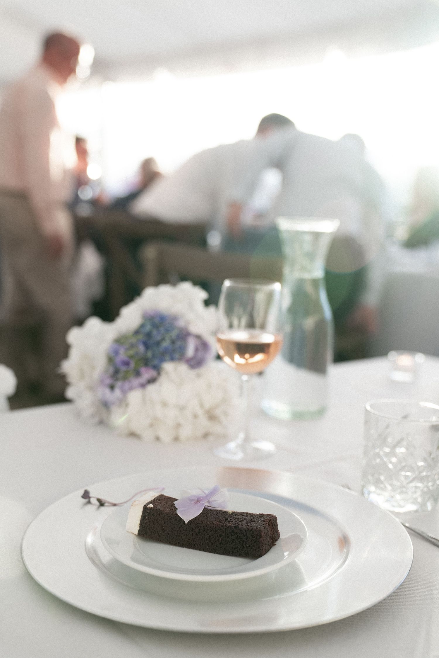 Elegant wedding reception table setting with white flowers, rose wine, and a chocolate brownie on a white plate.