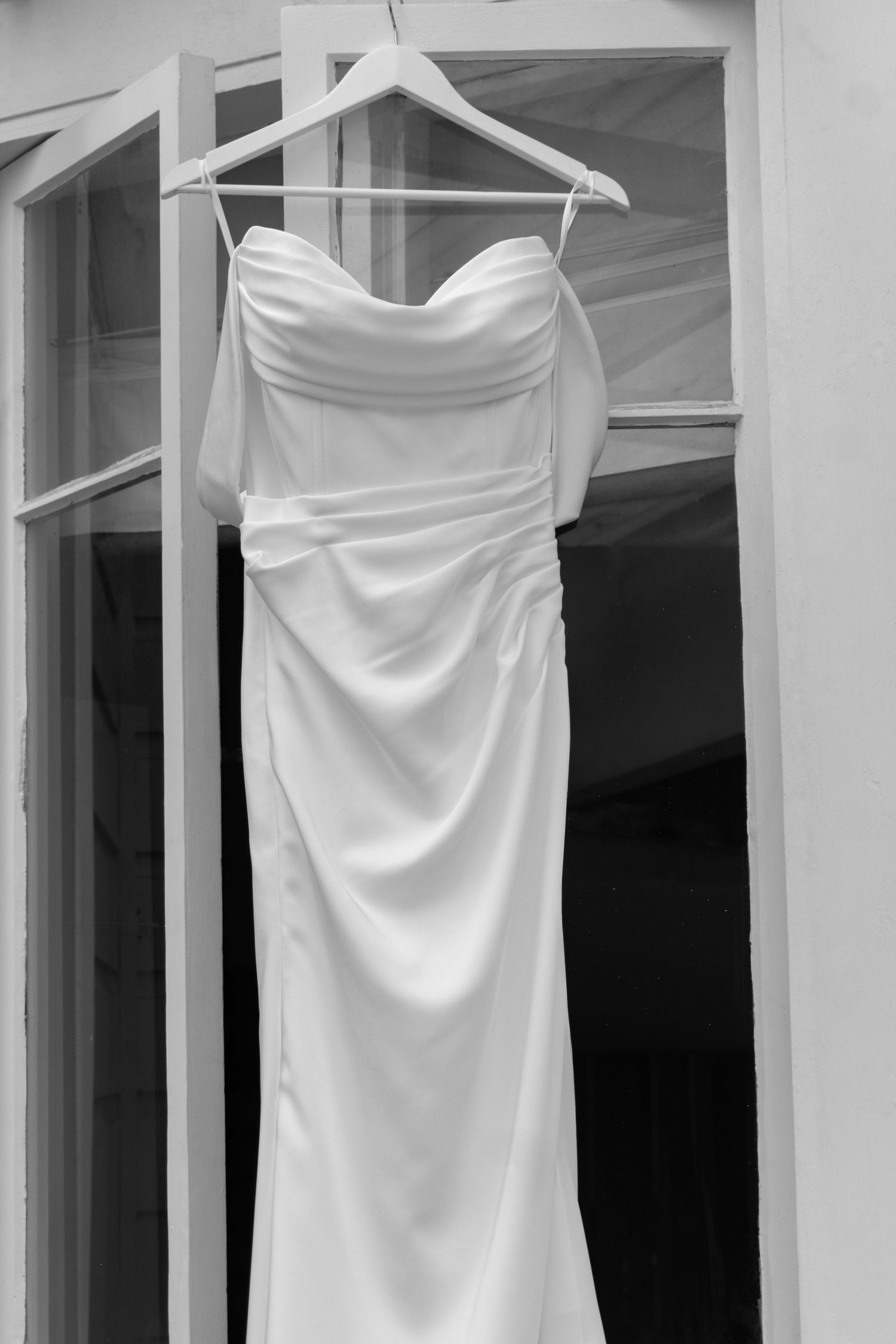 Elegant strapless white wedding dress hanging on a wooden hanger in a black and white photo.