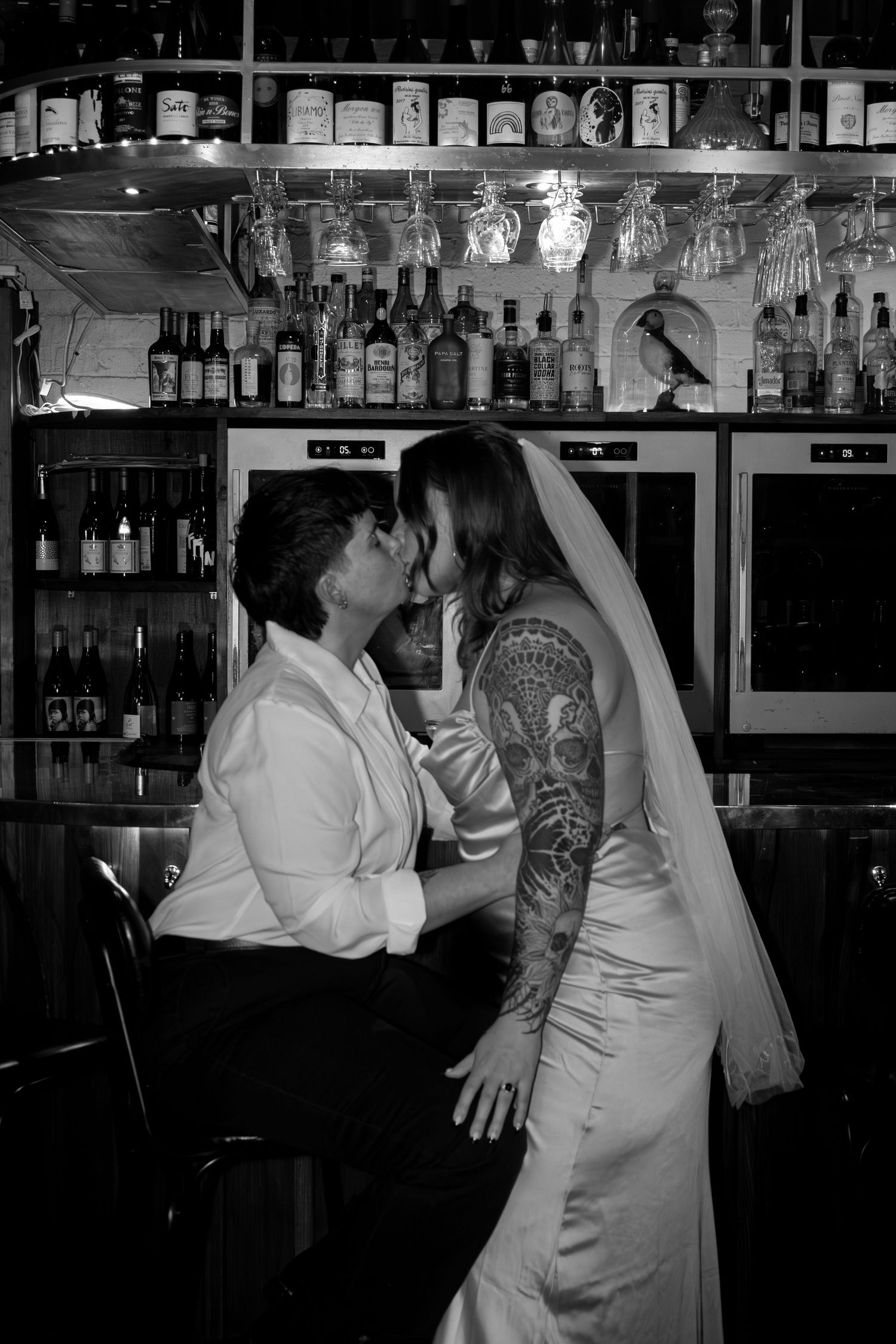 Black and white photo of tattooed bride and groom sharing a romantic kiss at a bar on their wedding day.