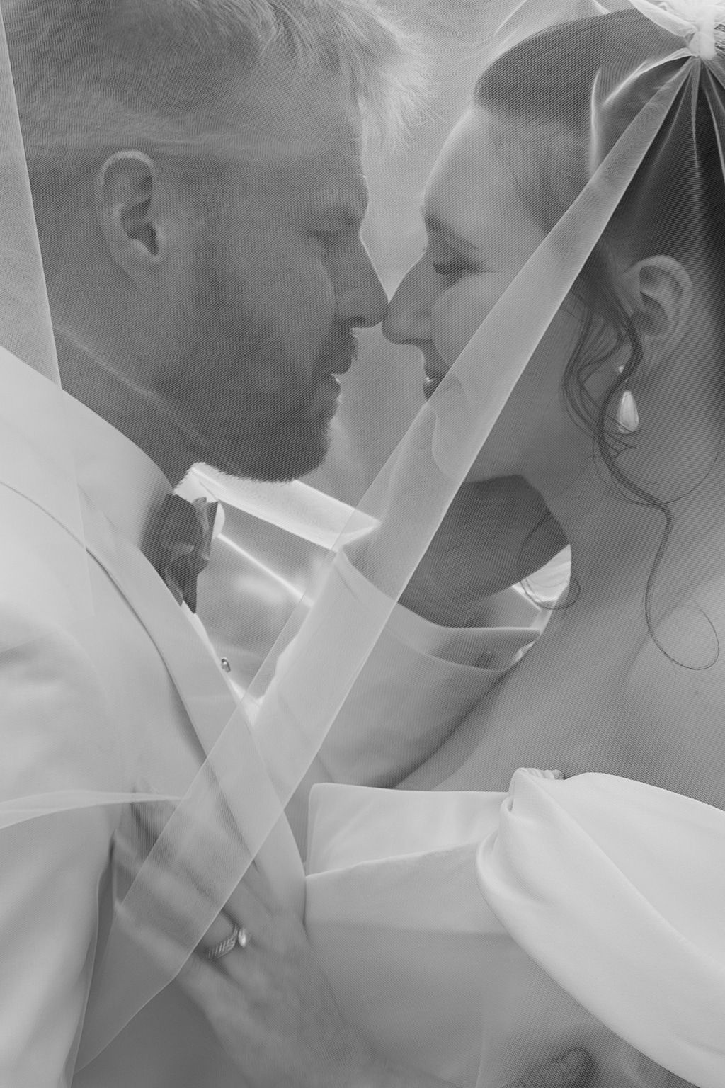 Black and white photo of a bride and groom sharing an intimate moment under a wedding veil.