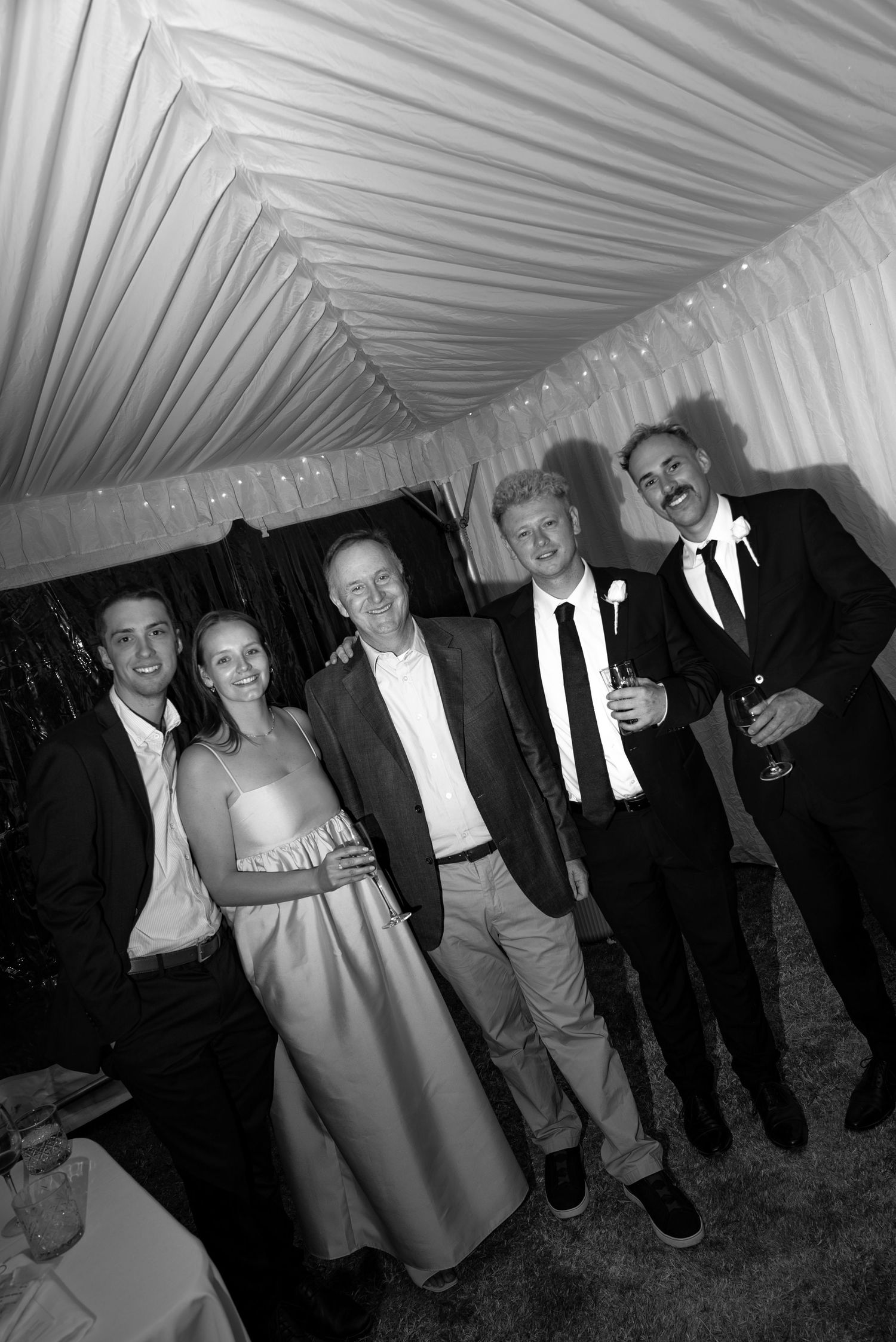 Black and white photo of five people posing together at a formal event inside a draped tent venue.