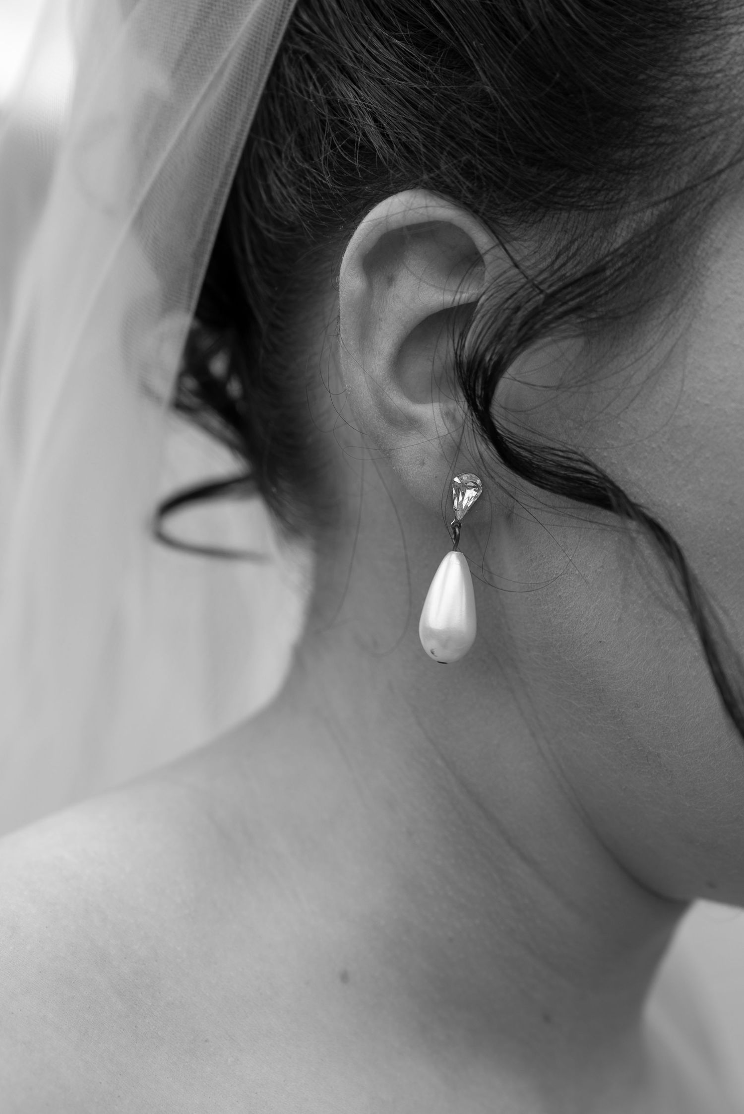 Black and white close-up of a bride wearing an elegant teardrop pearl earring with a diamond stud on her wedding day.