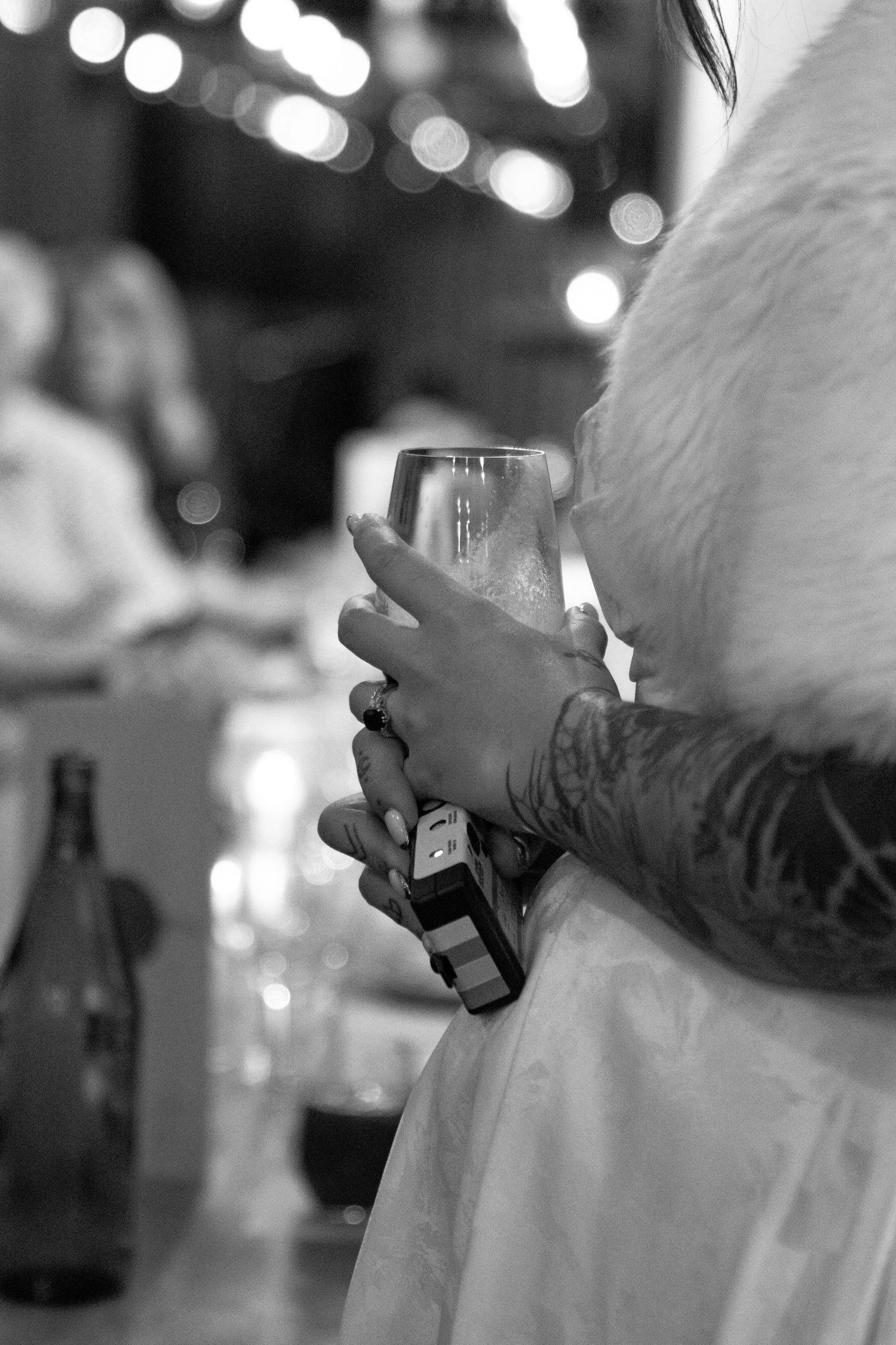 Black and white photo of a tattooed hand holding a champagne glass at an elegant party event.