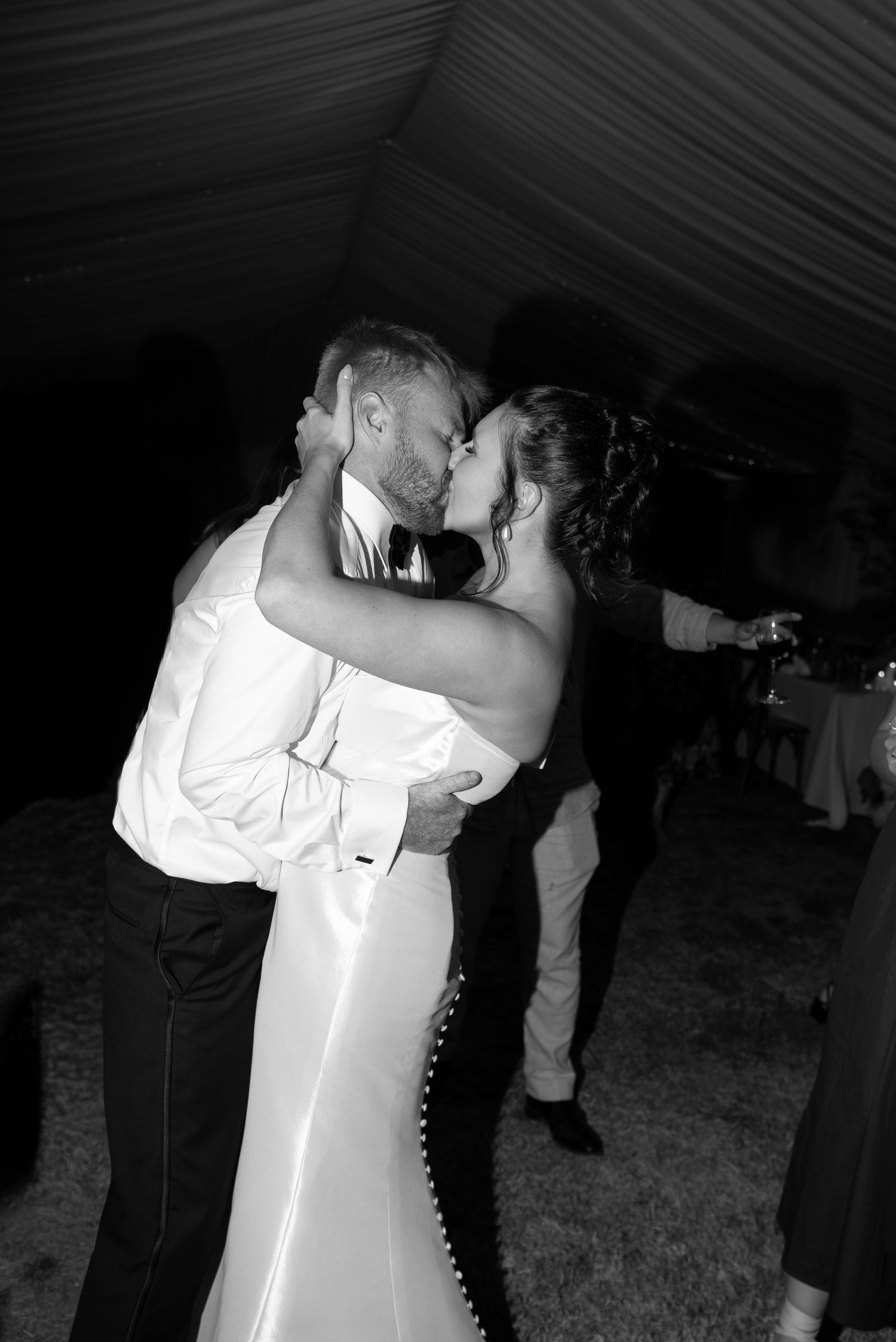 Black and white photo of a bride and groom sharing a kiss during their first dance at a wedding reception.