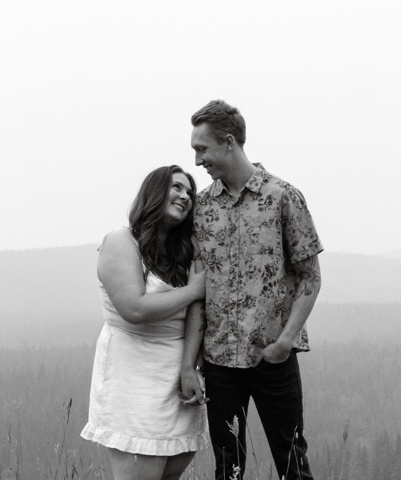 Couple shares tender moment in white against mountain backdrop.