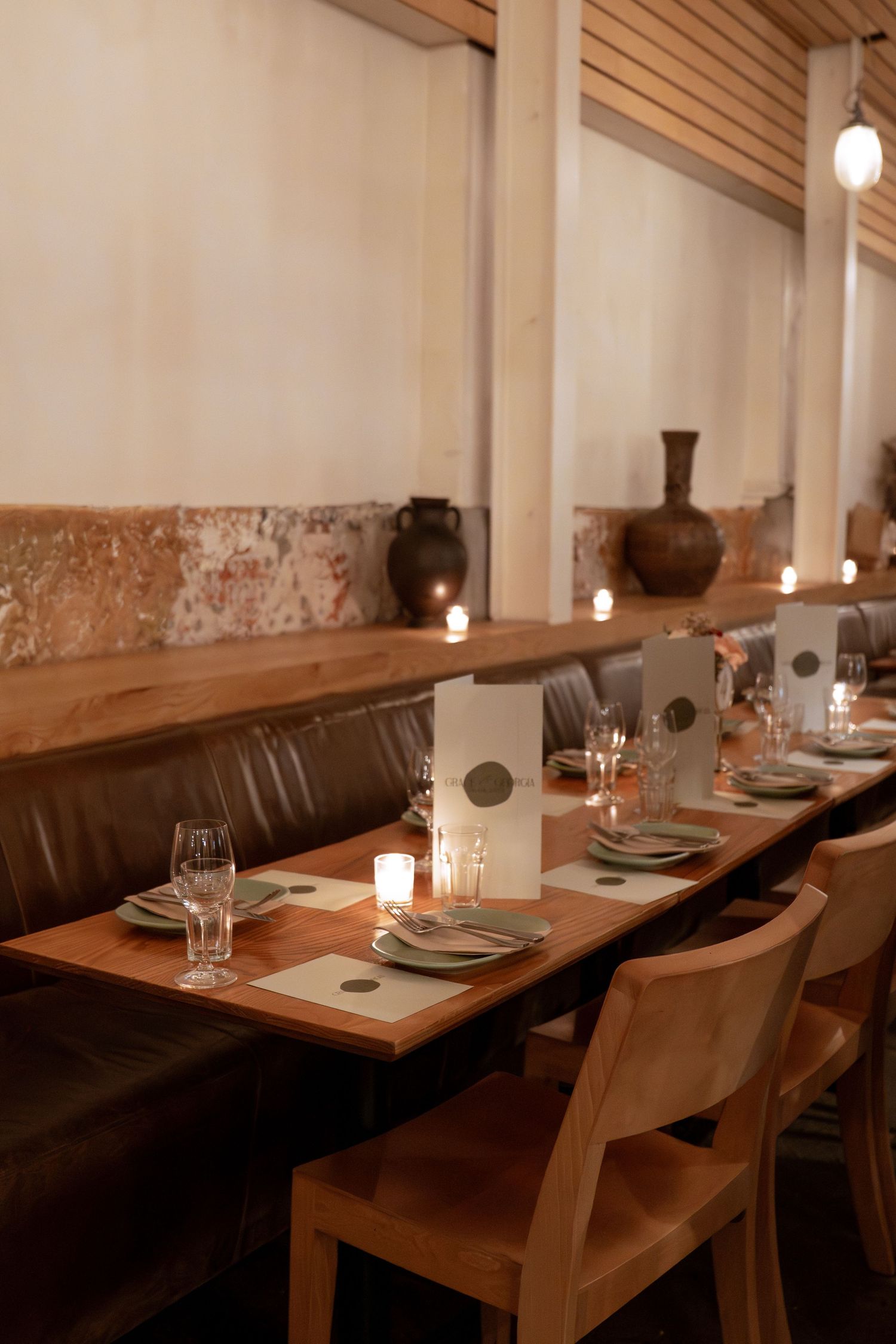 Elegant restaurant dining room with candlelit wooden tables, leather banquette seating, and warm ambient lighting.